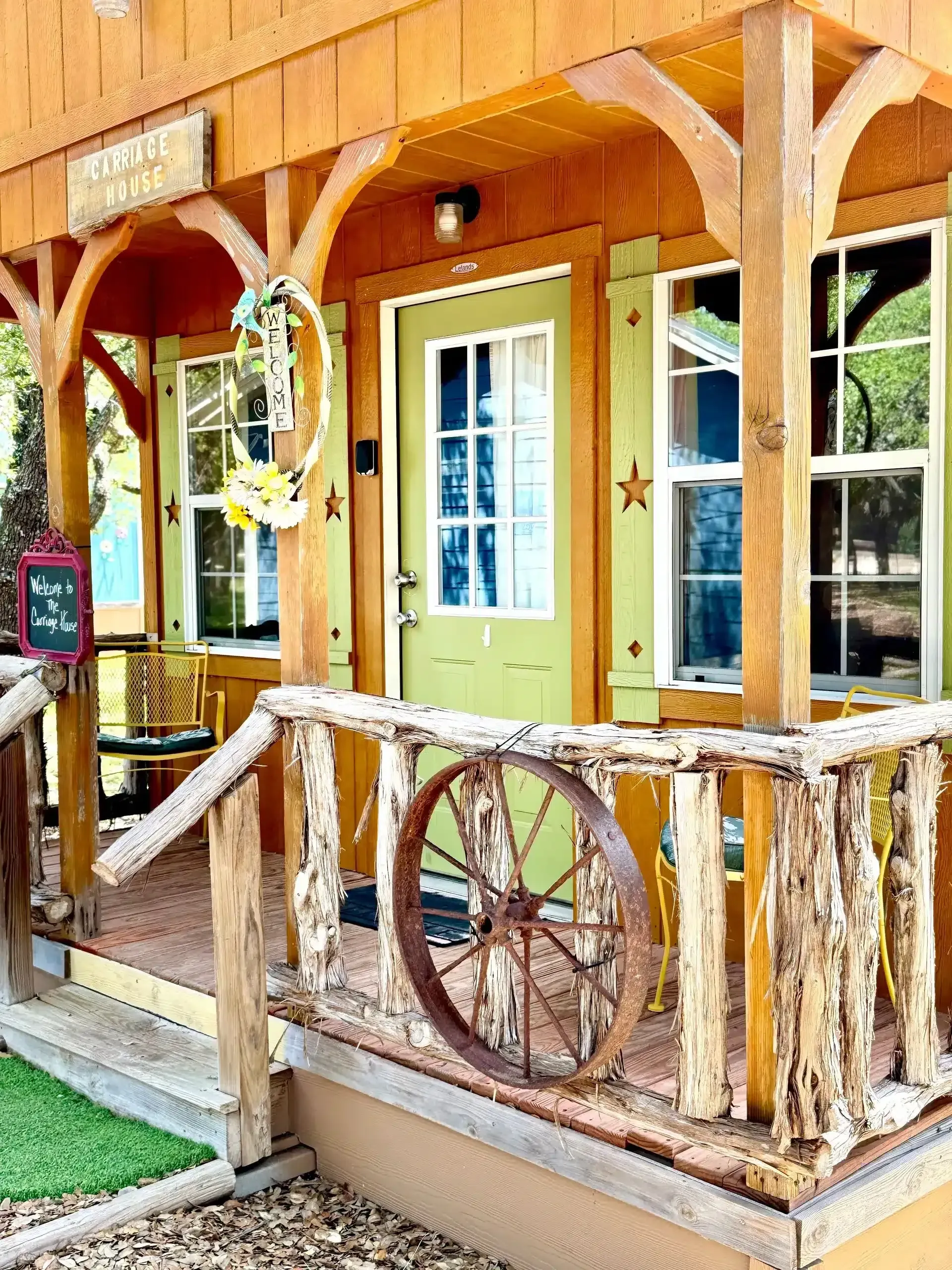 Rustic wooden porch with wagon wheel railing and a yellow door on a small cabin.