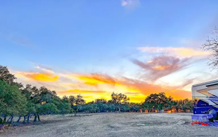 Sunset over a tree-lined field with vivid orange and purple clouds