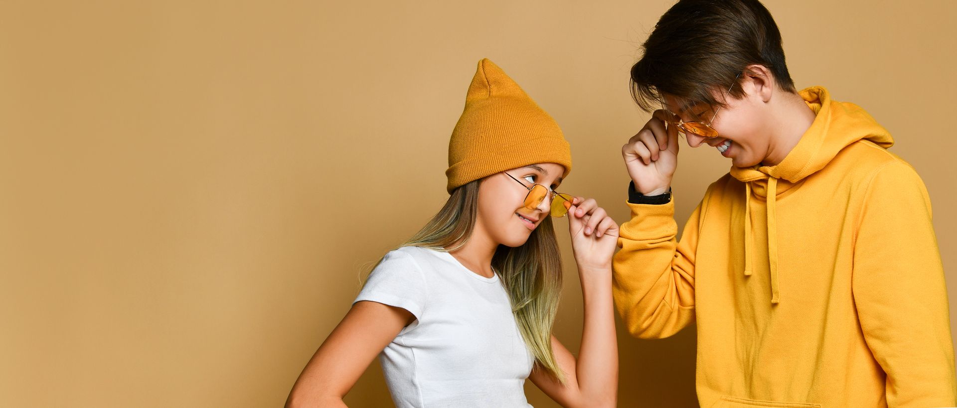 A boy and a girl are standing next to each other on a yellow background.