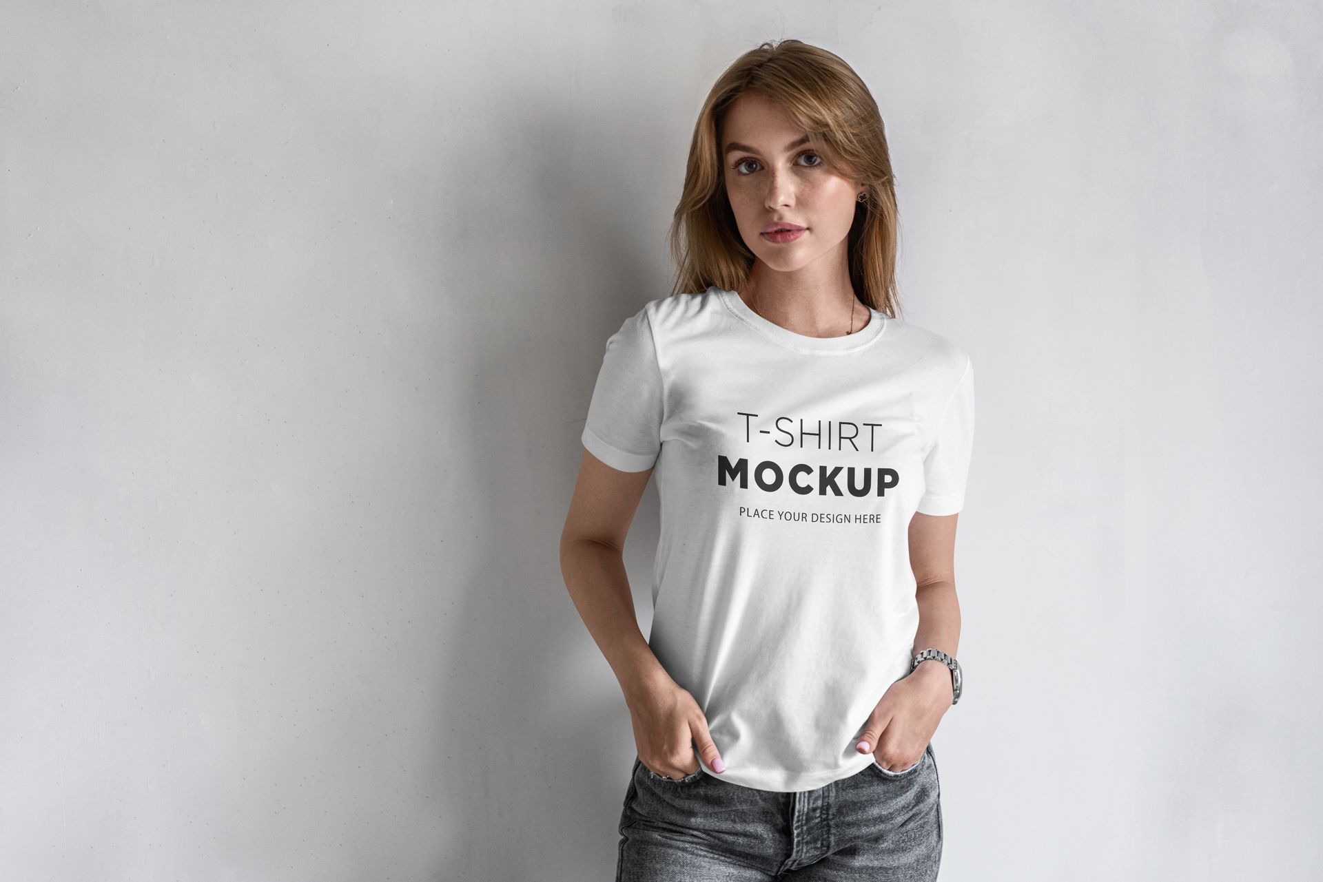 A woman wearing a white t-shirt mockup is standing in front of a white wall.
