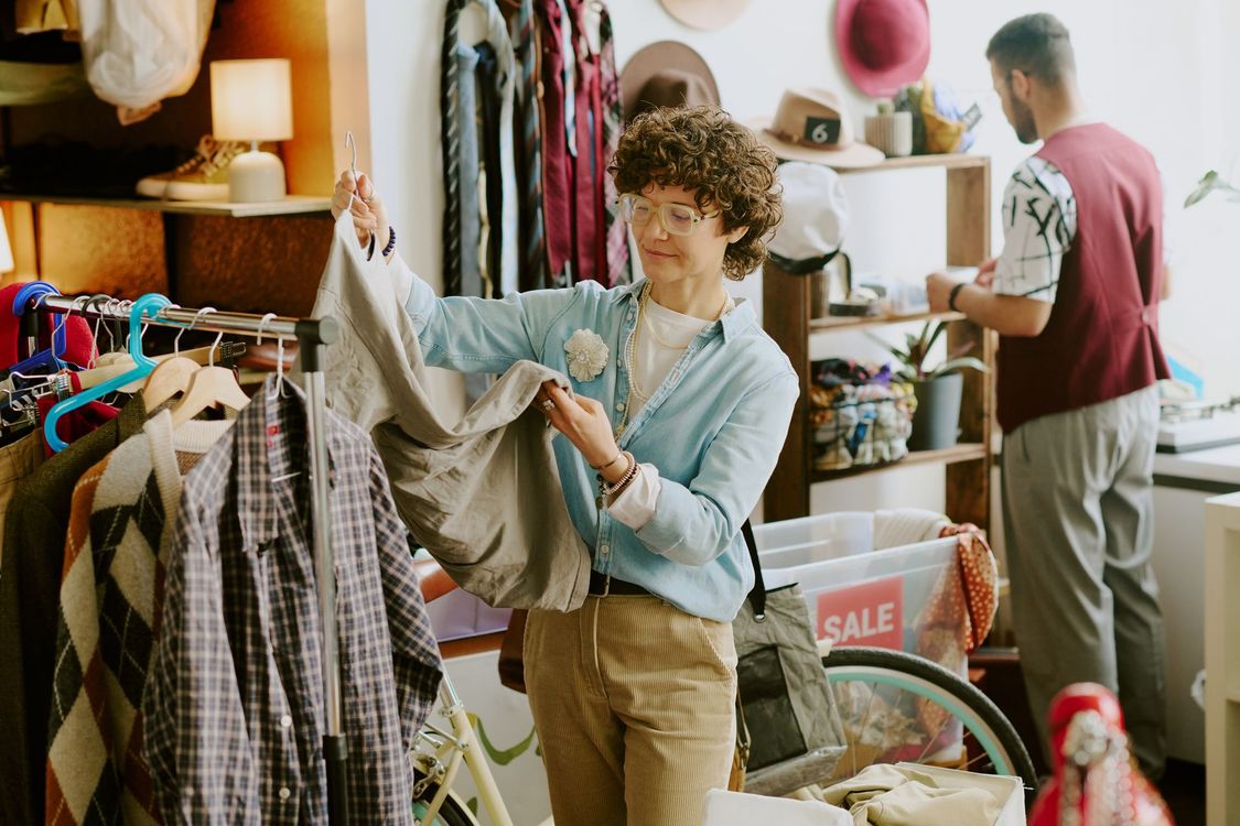 A woman is holding a piece of clothing in a thrift store.