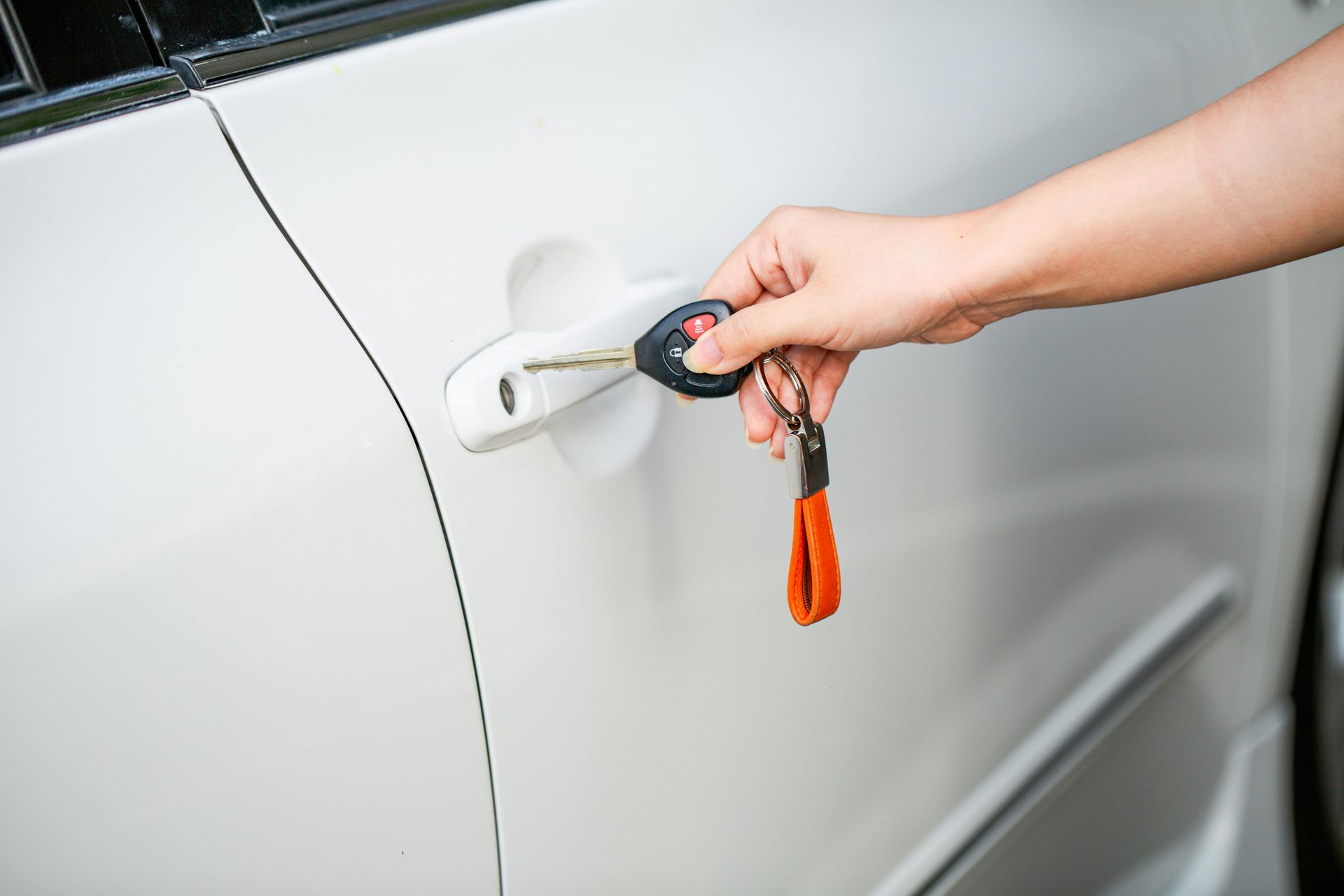 A hand uses a car key to unlock the door handle of a white vehicle.