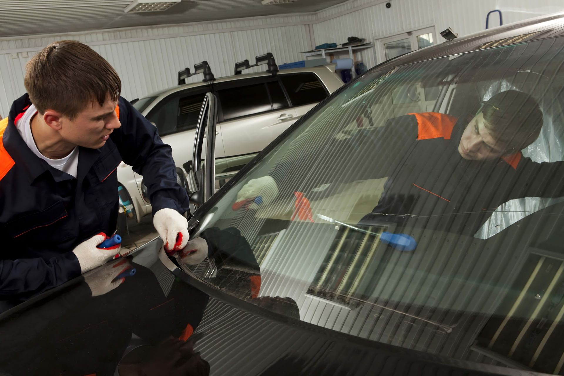two men are working on a car windshield in a garage .
