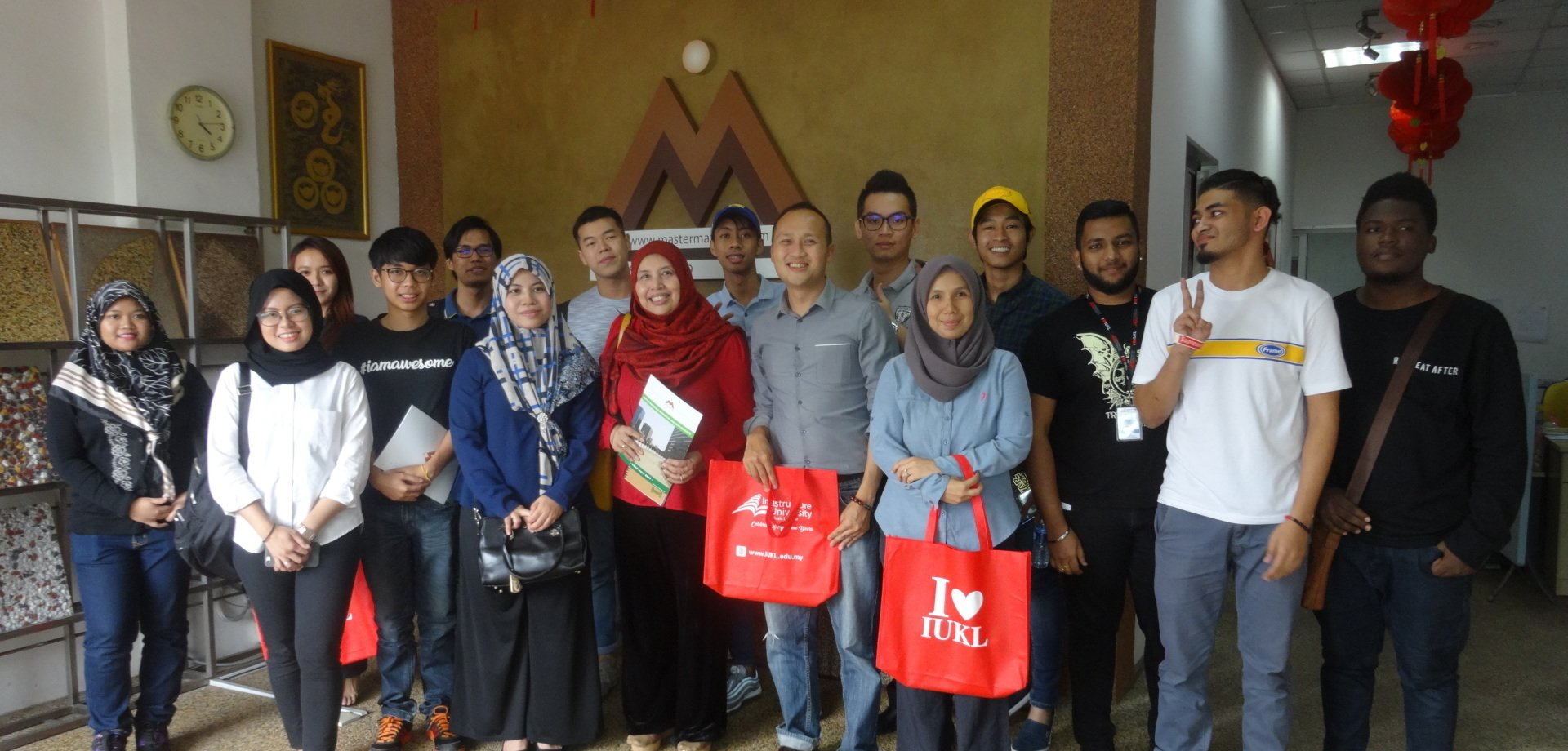 A group of people posing together inside a building. Some are holding red shopping bags. A logo is on the wall.