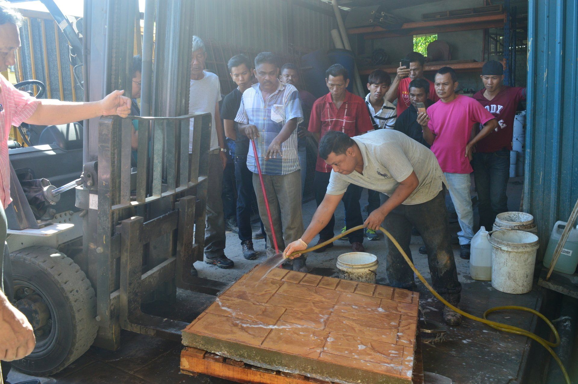 A man hoses a large square object on a pallet, surrounded by a group of people.