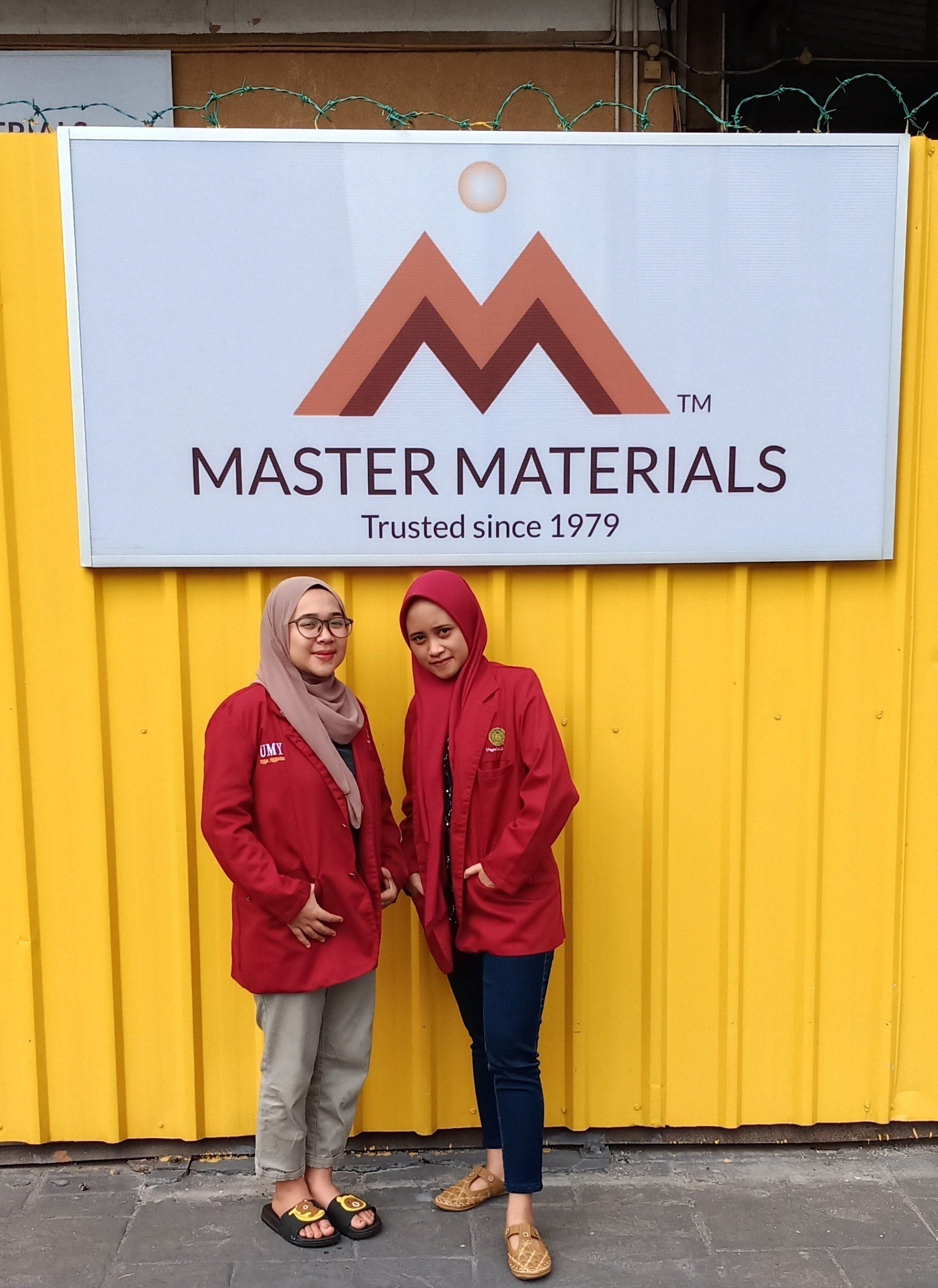 Two women in red jackets stand in front of a 