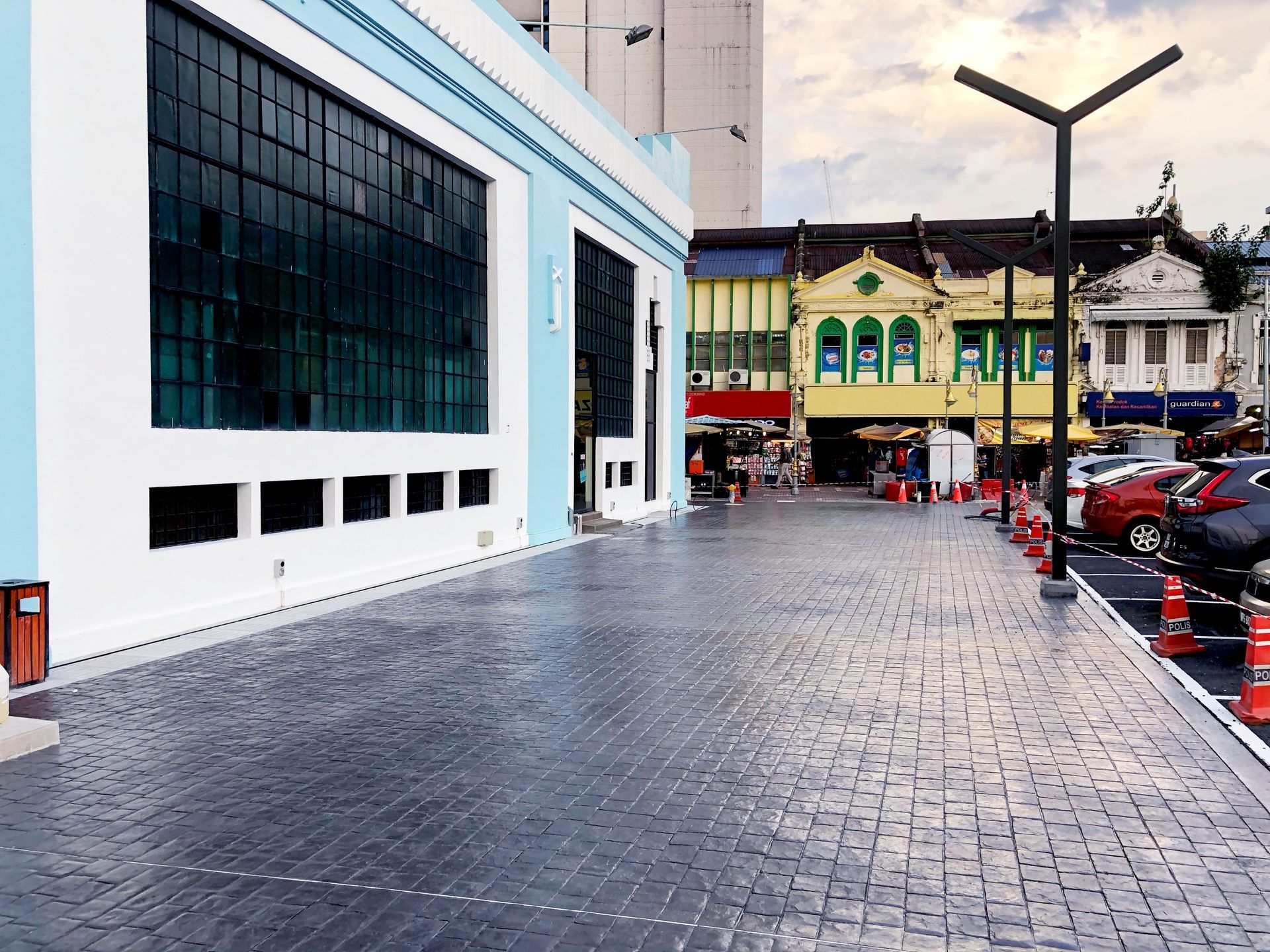 View of a gray paved plaza with blue and white building on the left and colorful buildings in the background. 