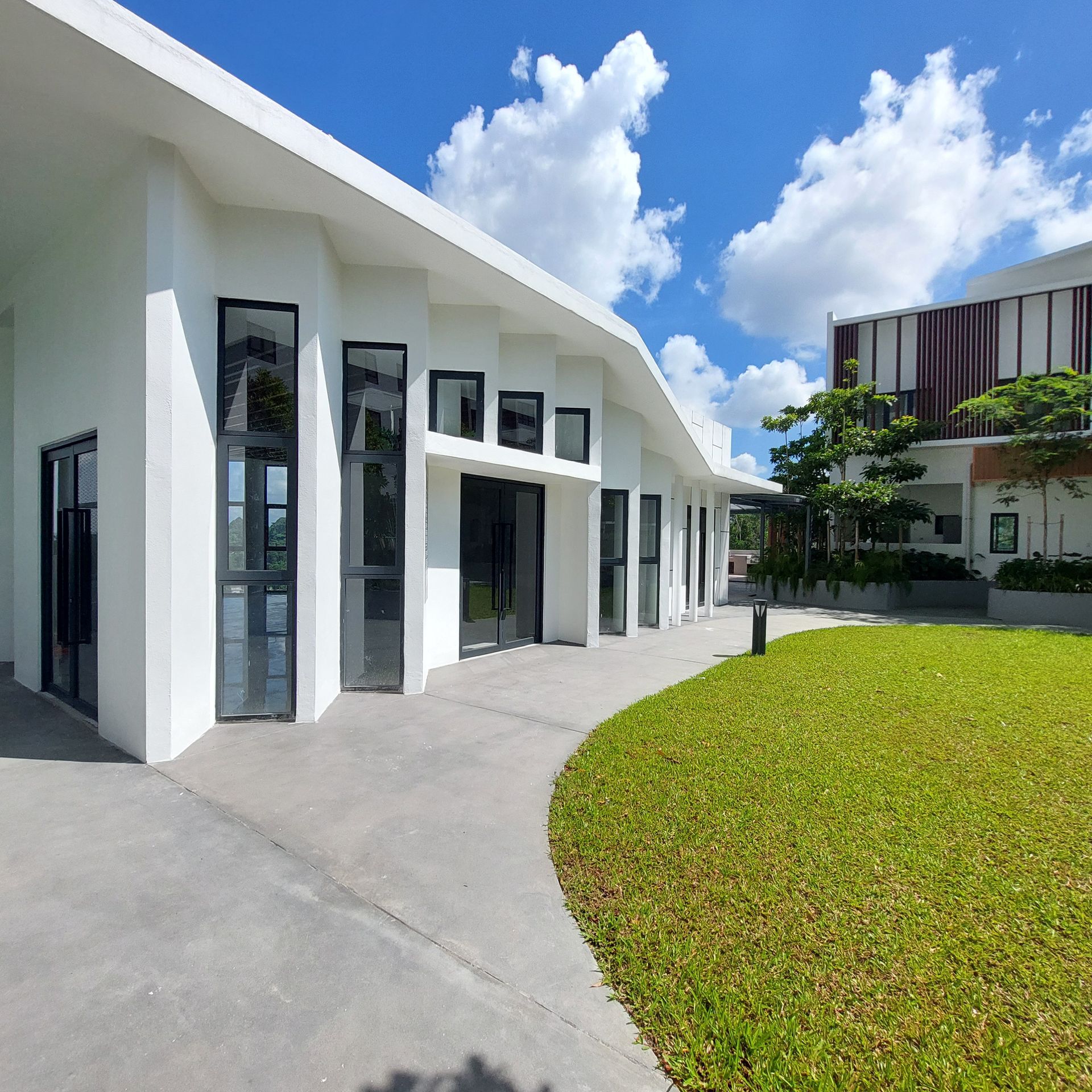 White building with black-framed windows, walkway, and green lawn under a blue sky with clouds.