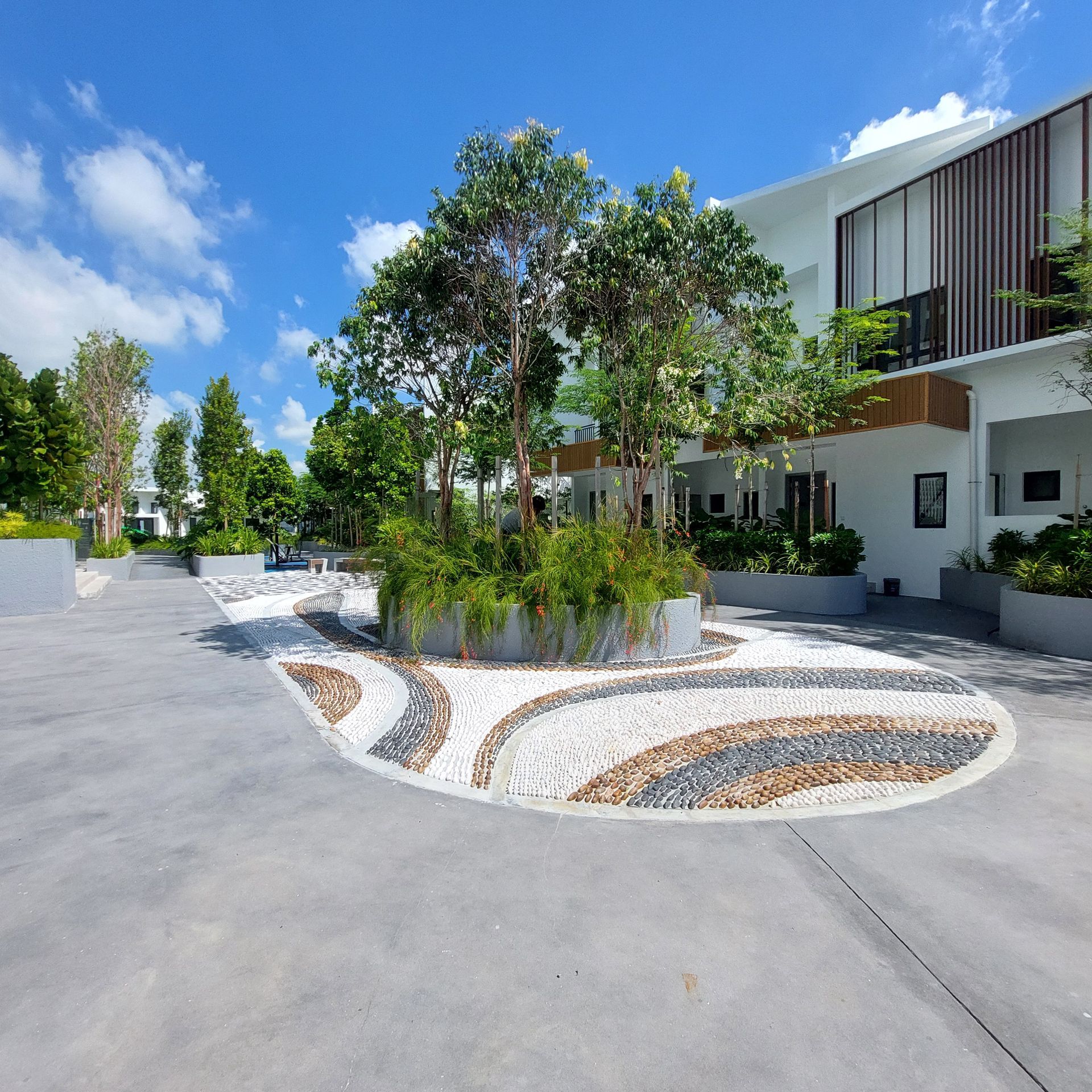 A modern building exterior with a decorative stone and tree garden area, against a bright blue sky.