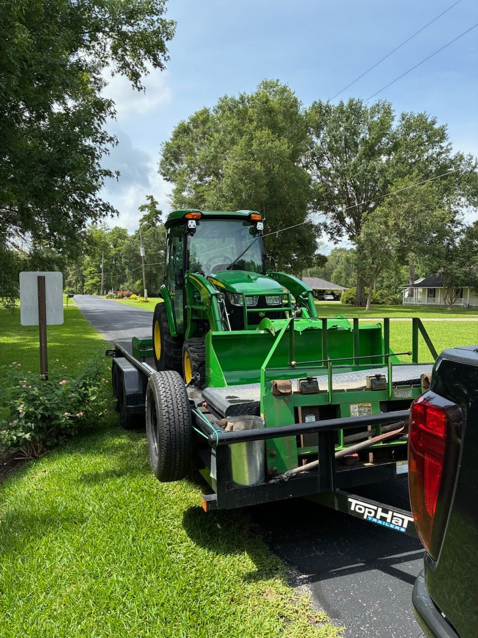 A green tractor is on a trailer attached to a truck.