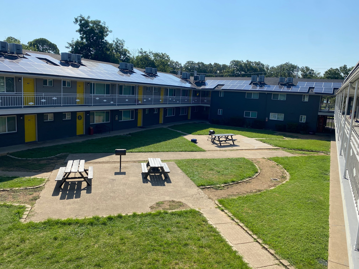 Courtyard apartment complex with green grass, picnic tables, and dark buildings with solar panels.