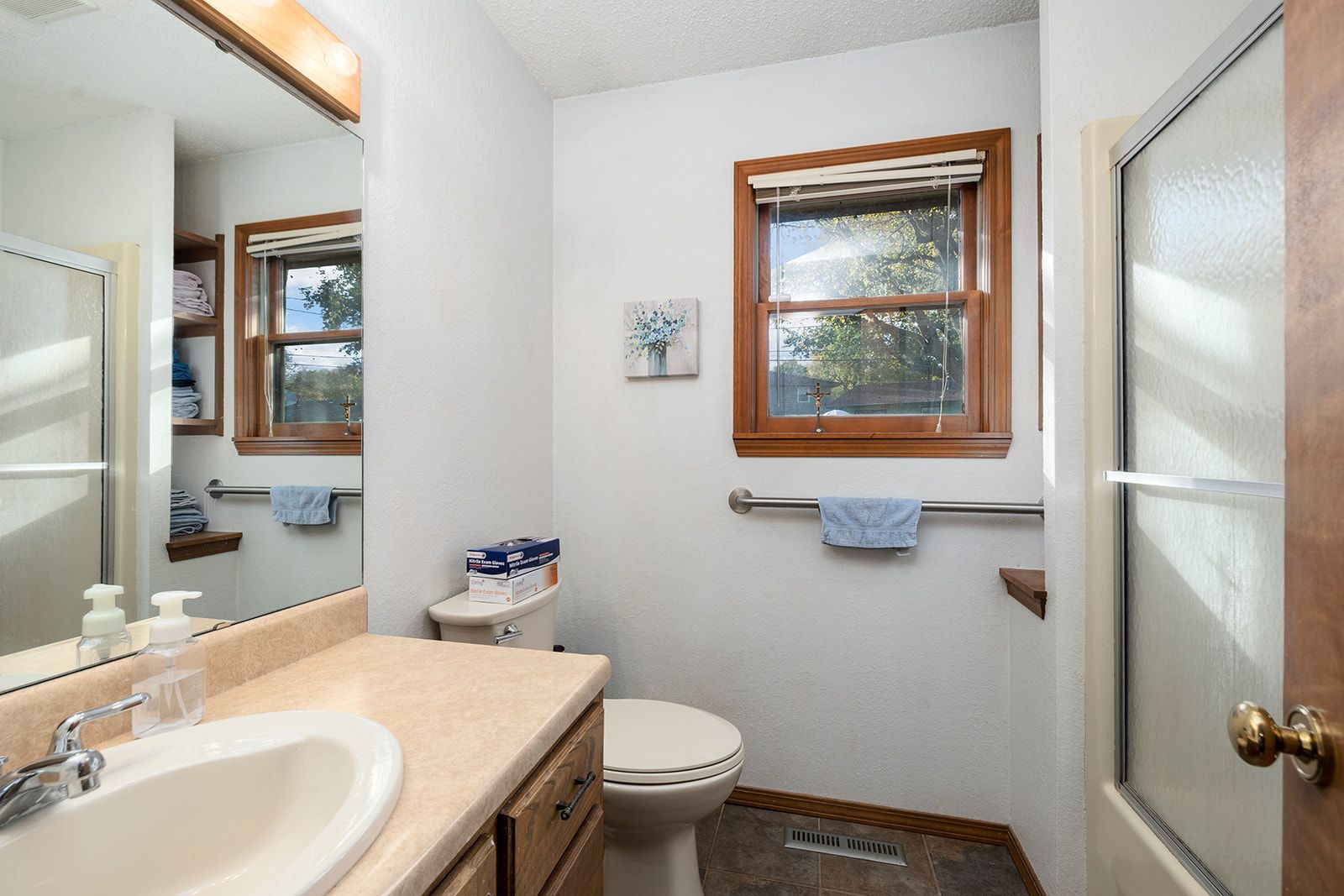 A bathroom with a toilet , sink , mirror and window.