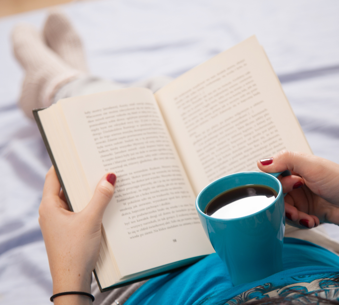 A woman is reading a book next to a cup of coffee