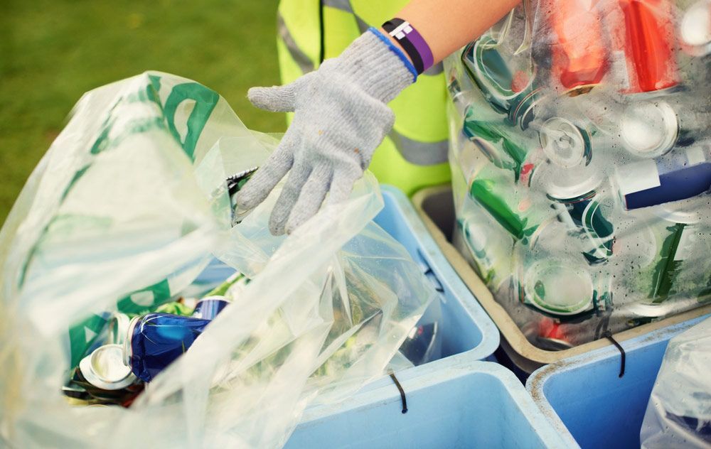 A Person Wearing Gloves is Putting a Plastic Bag Into a Recycling Bin — Handi Skips in Bohle, QLD