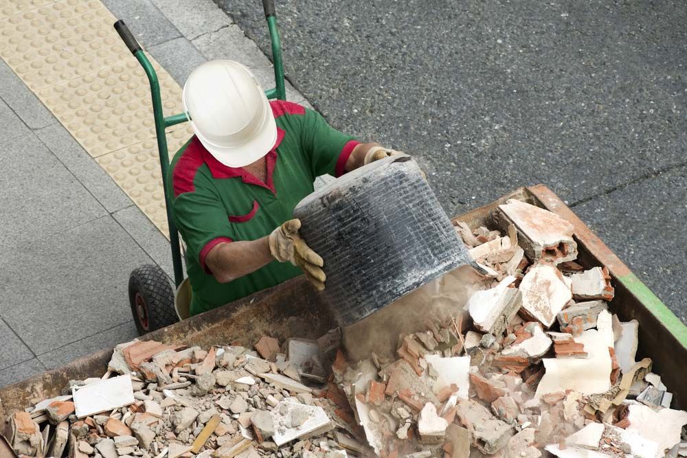 A Man Wearing a Hard Hat is Pushing a Cart Full of Bricks — Handi Skips in Bohle, QLD