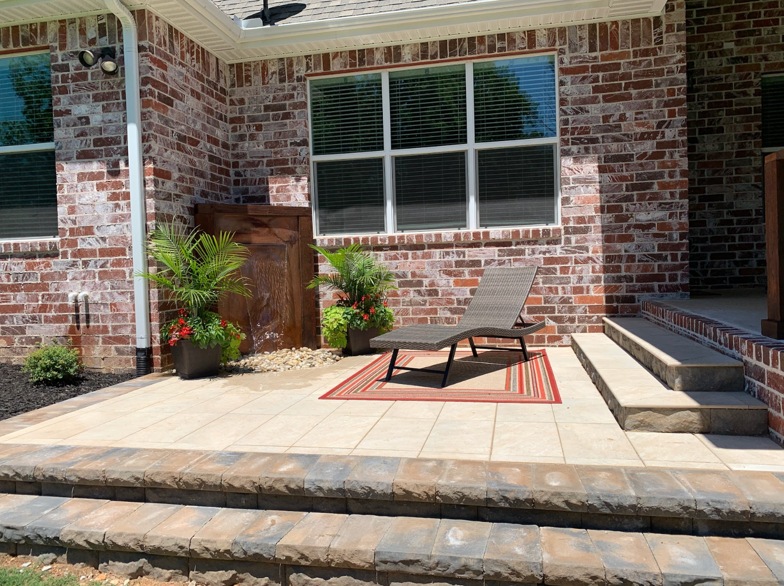 A patio with a chair and a rug in front of a brick house.