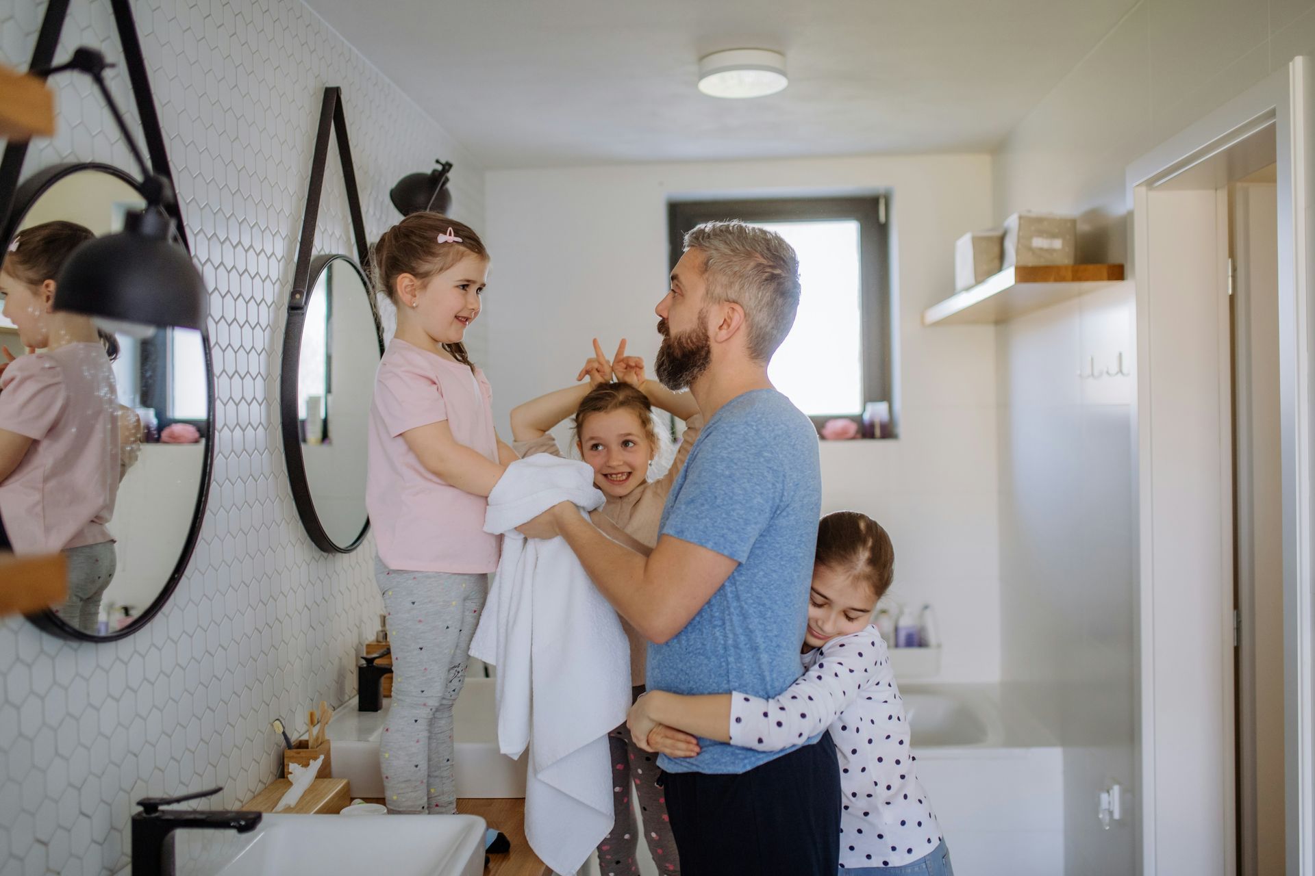 A man and two little girls are standing in a bathroom.