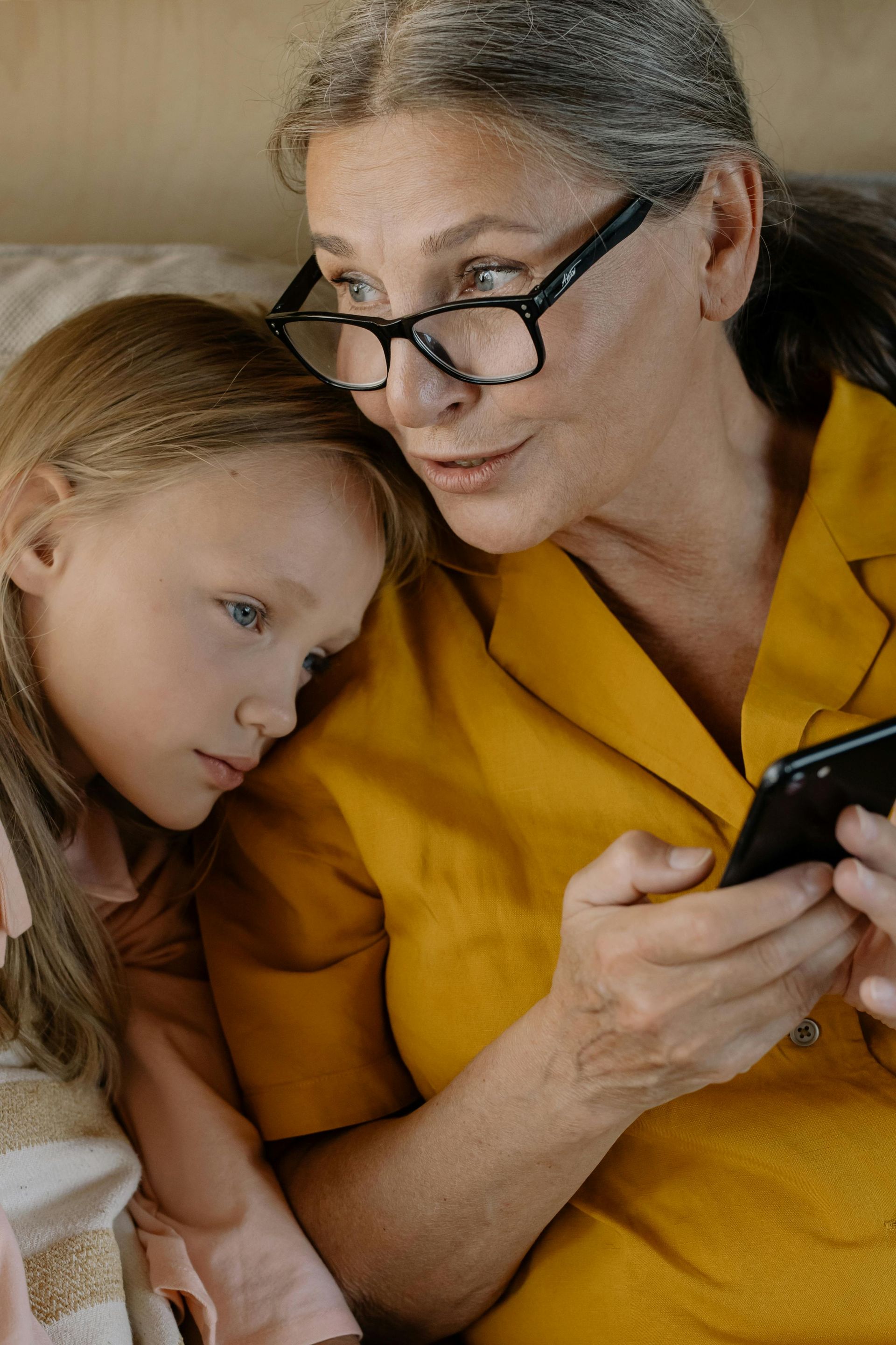 An elderly woman and a little girl are looking at a cell phone.