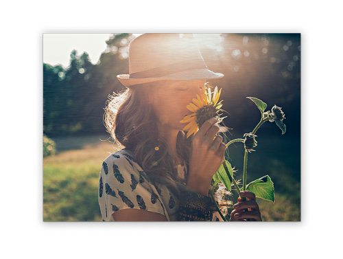 A woman in a hat is smelling a sunflower in a field.