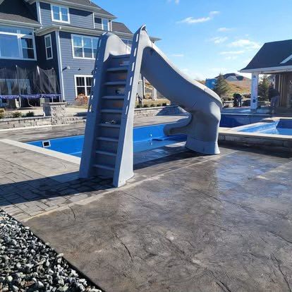 Blue pool slide beside a house, with a ladder and curved chute on a wet patio.