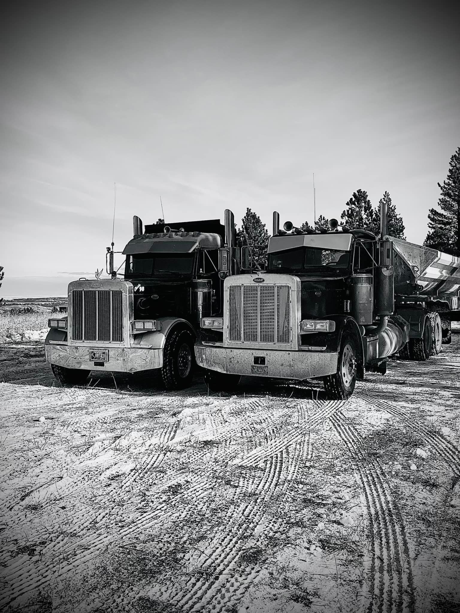 Two semi-trucks parked in a snow-covered area. Black and white photo.