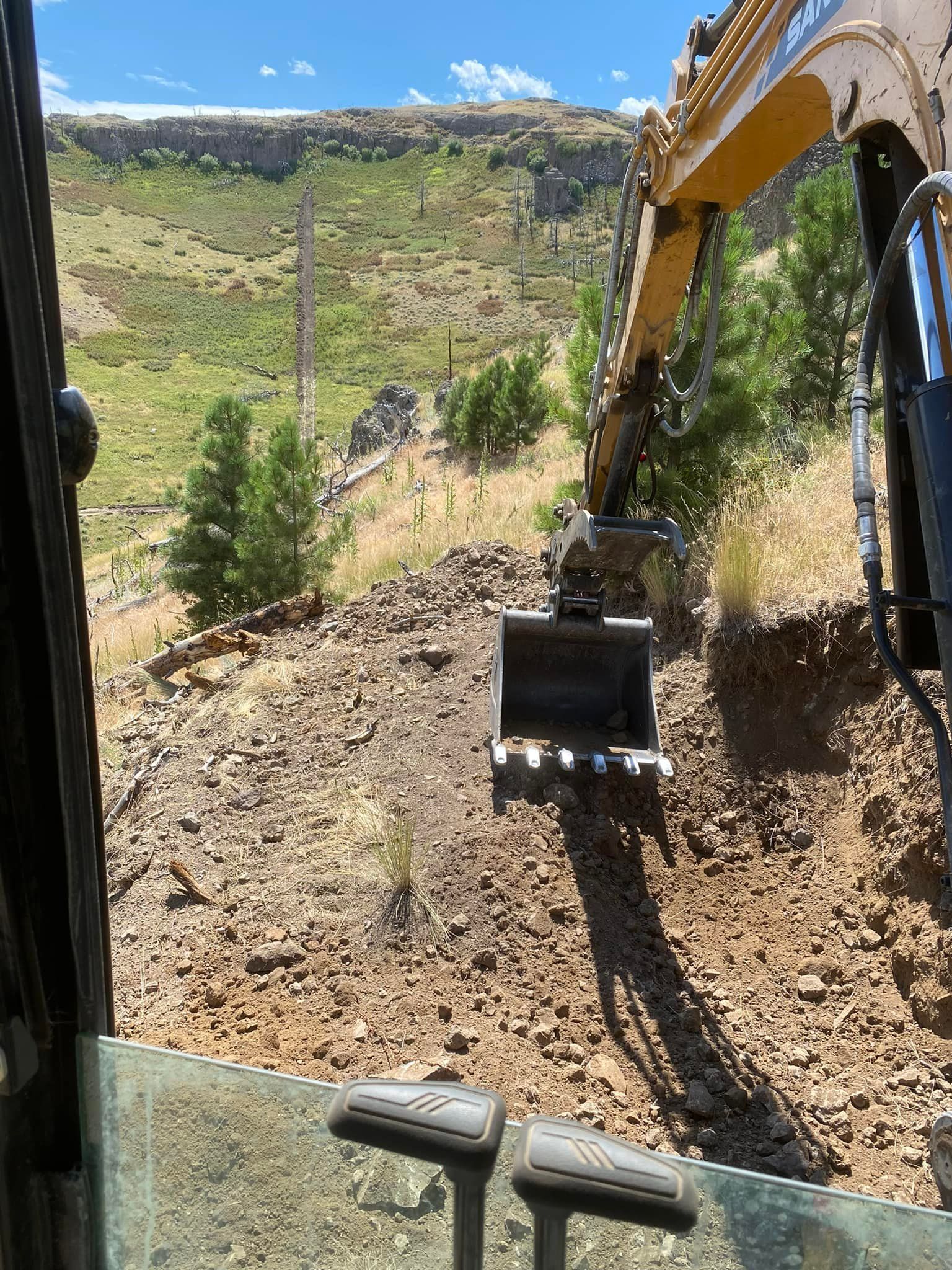 Excavator bucket scooping earth from a hillside. Sunlit scene.