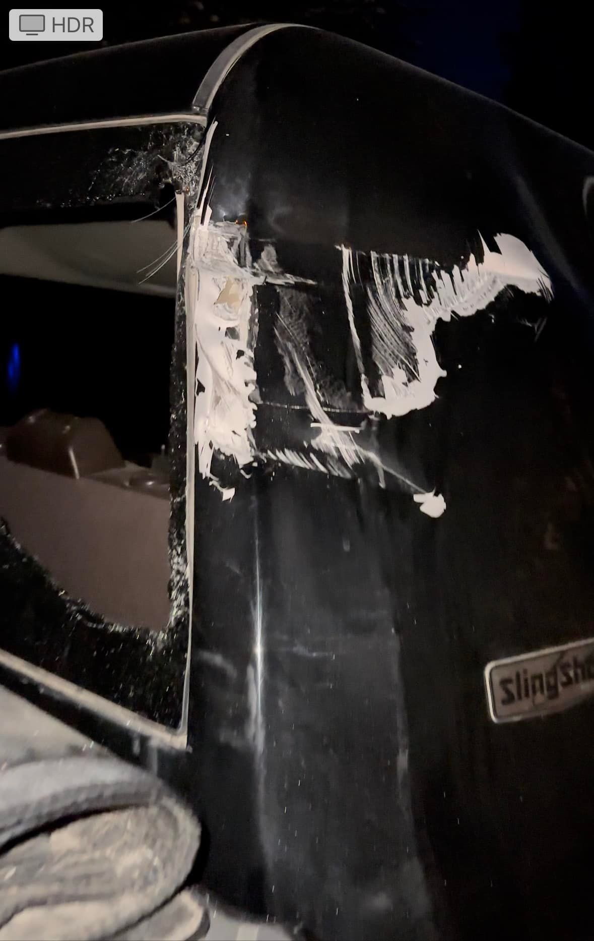 Damaged black vehicle side with white paint splatters and broken window; 