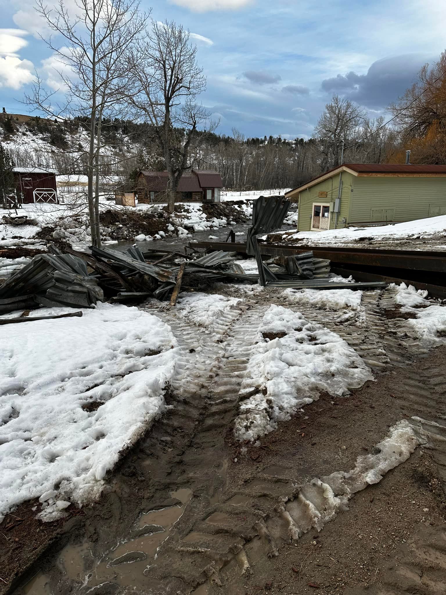 Snowy outdoor scene; melting snow, muddy ground. Buildings, trees and overcast sky visible.