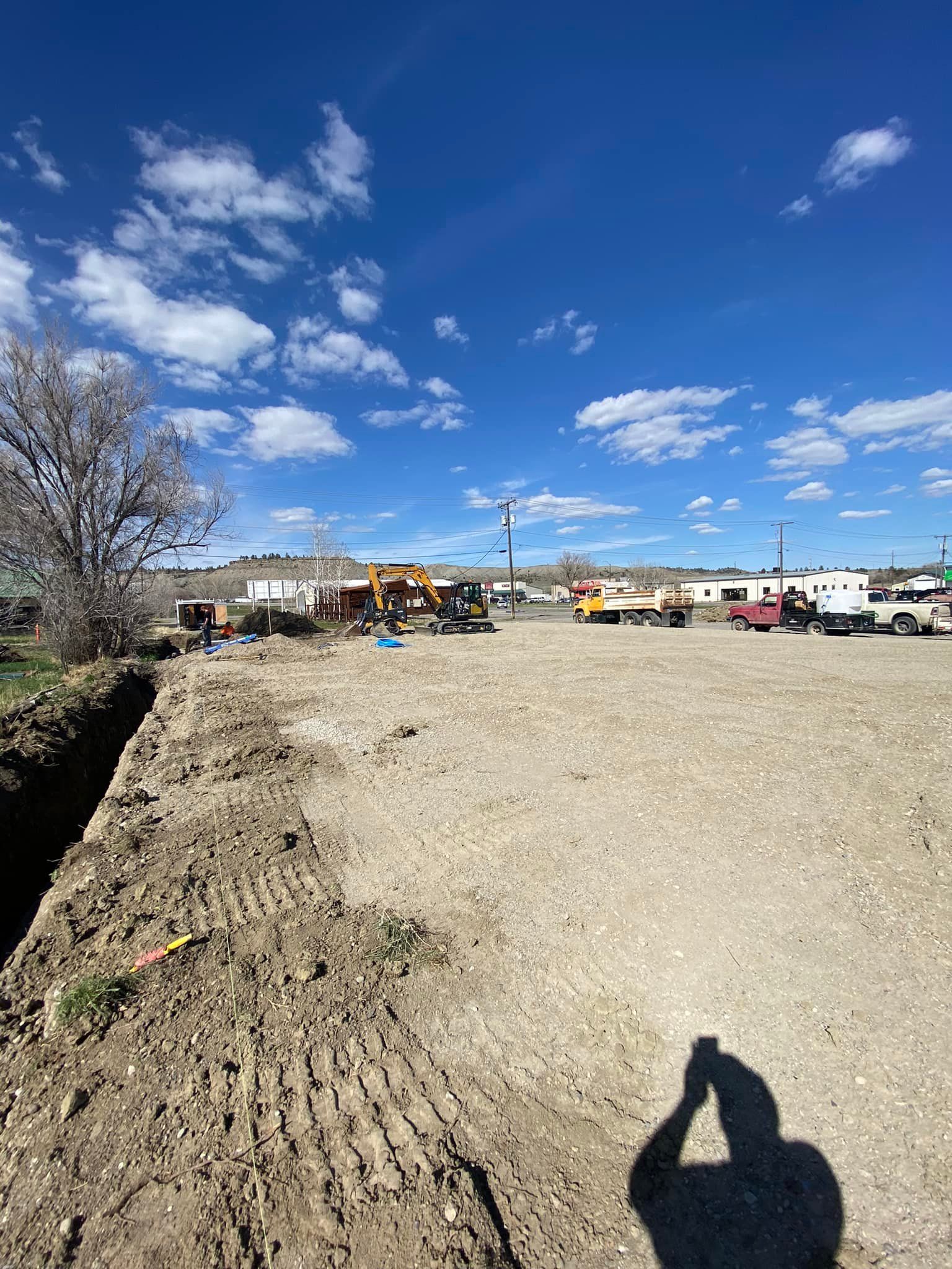 Construction site on a sunny day. Dirt, machinery, blue sky with clouds. Shadow of person taking photo.