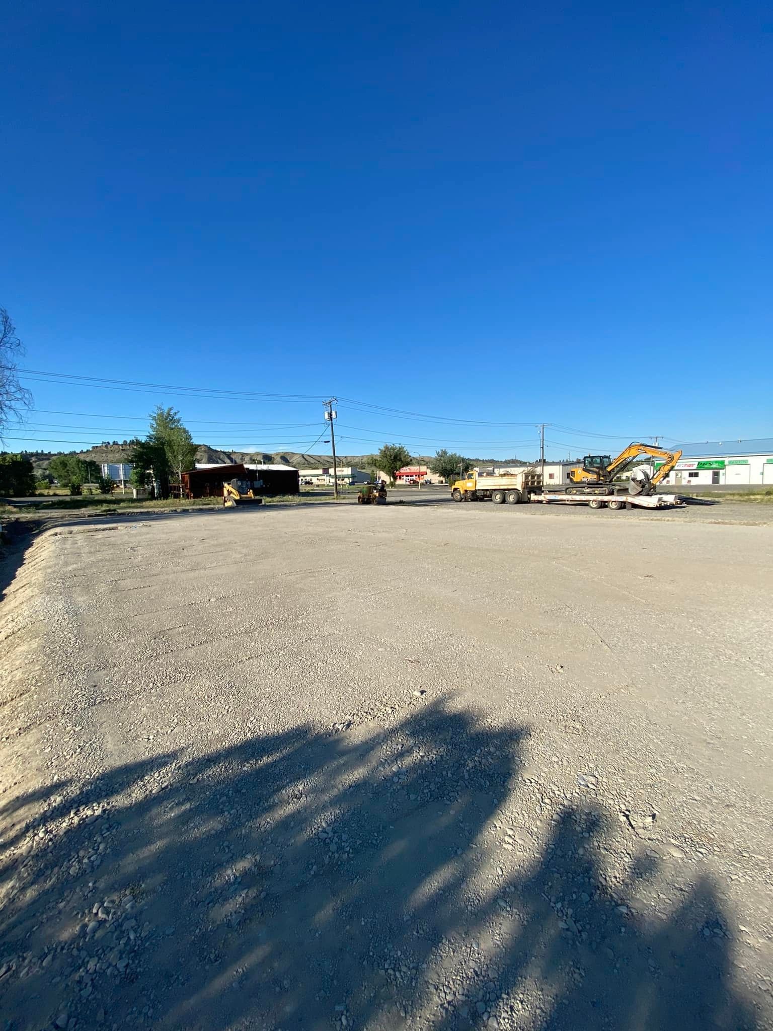 Gravel lot under a blue sky, construction equipment in the distance.