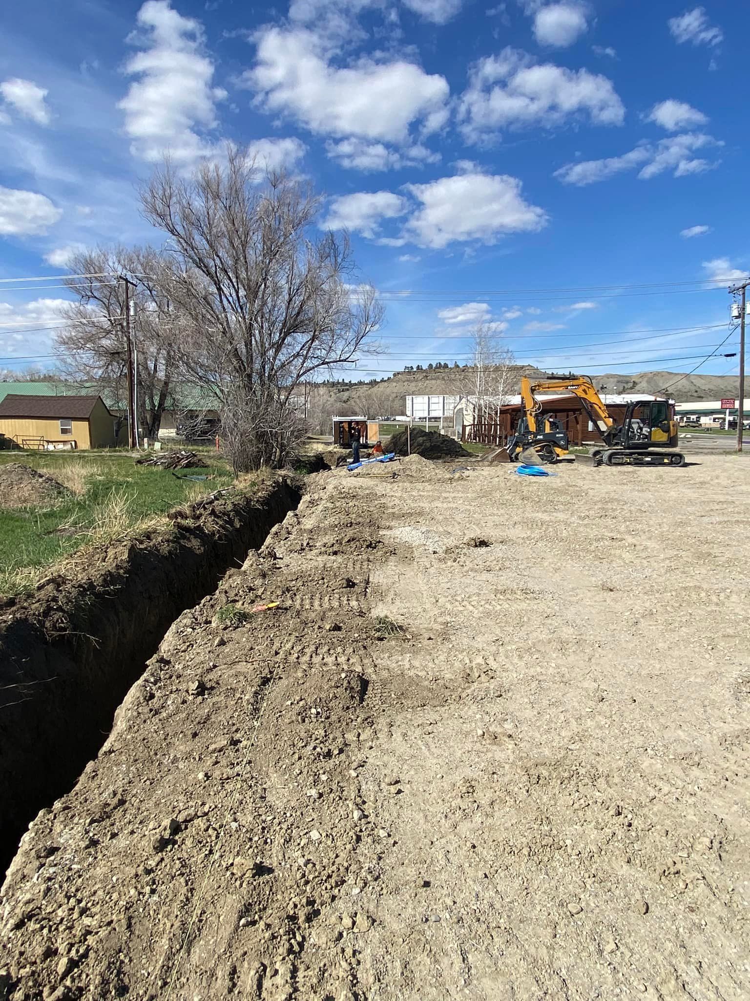 Construction site with an excavated trench, machinery, and a cloudy sky.