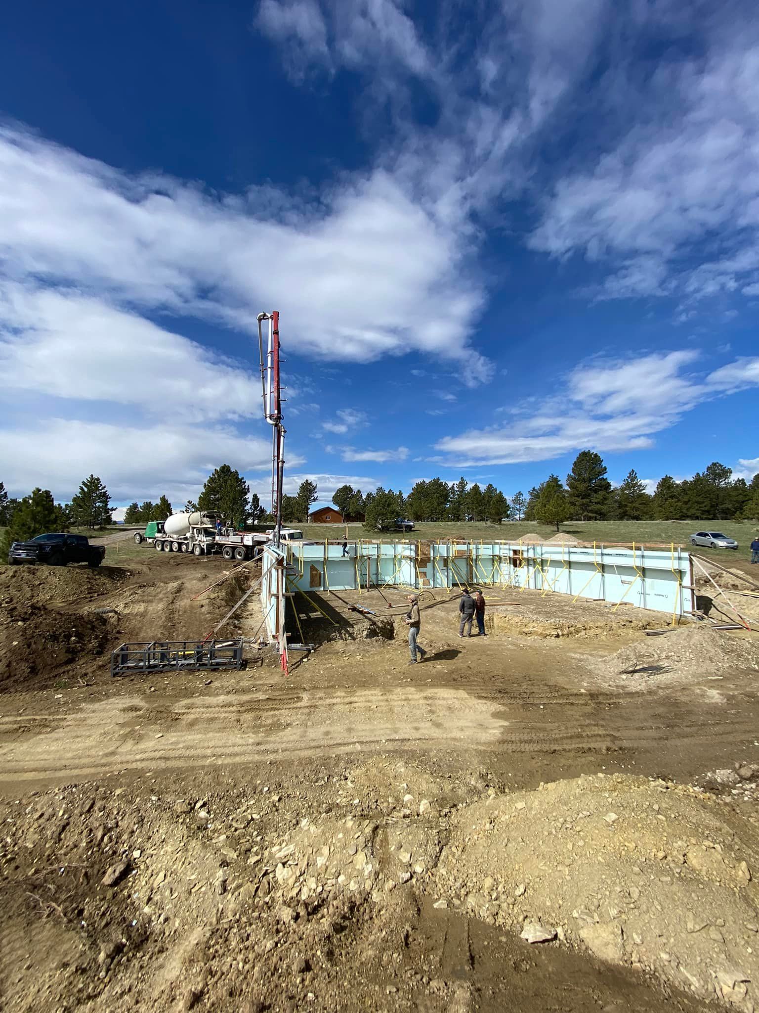 Construction site with concrete pump truck filling insulated concrete form walls against a blue sky.