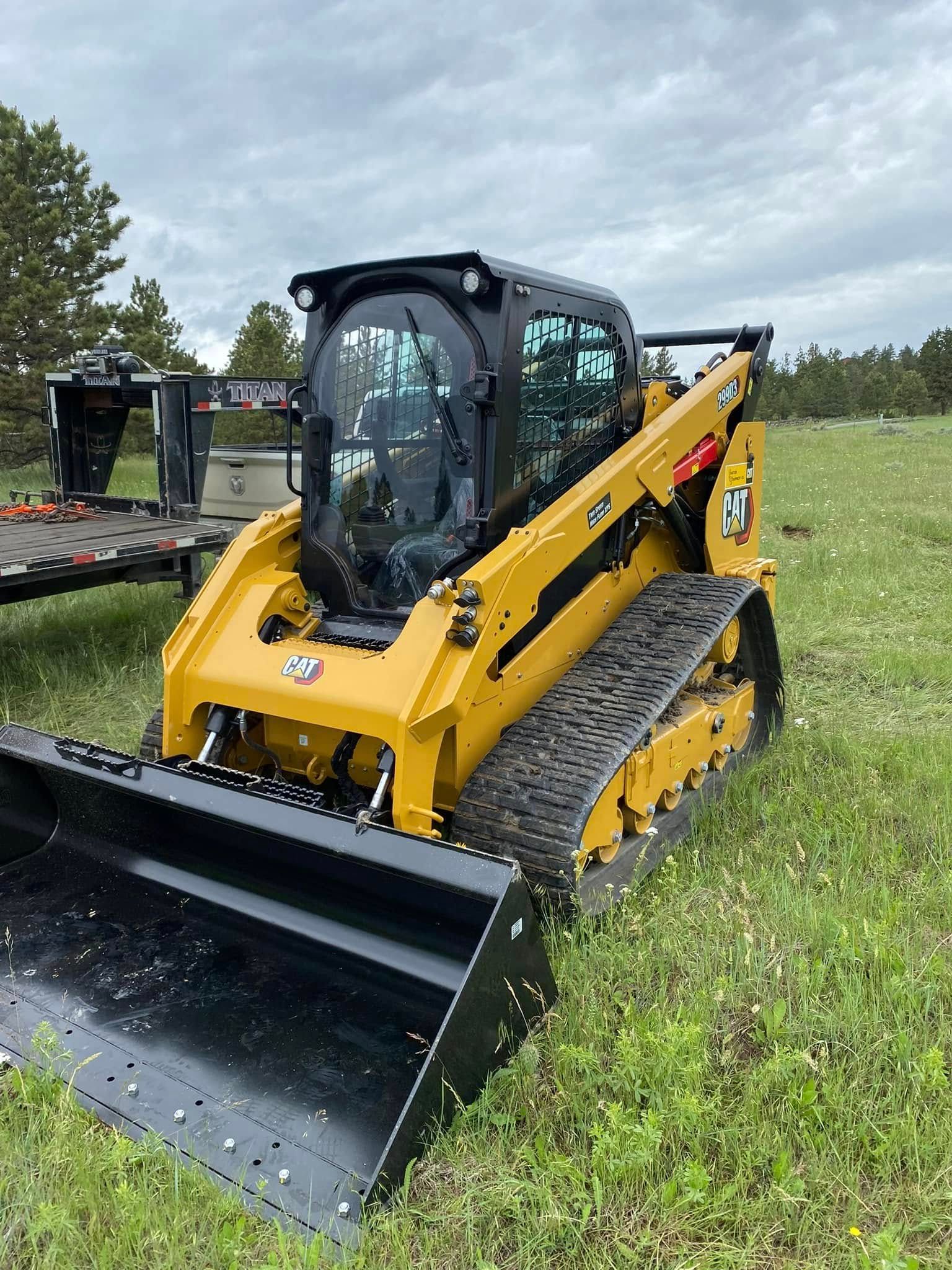 Yellow and black Caterpillar compact track loader in a grassy field.