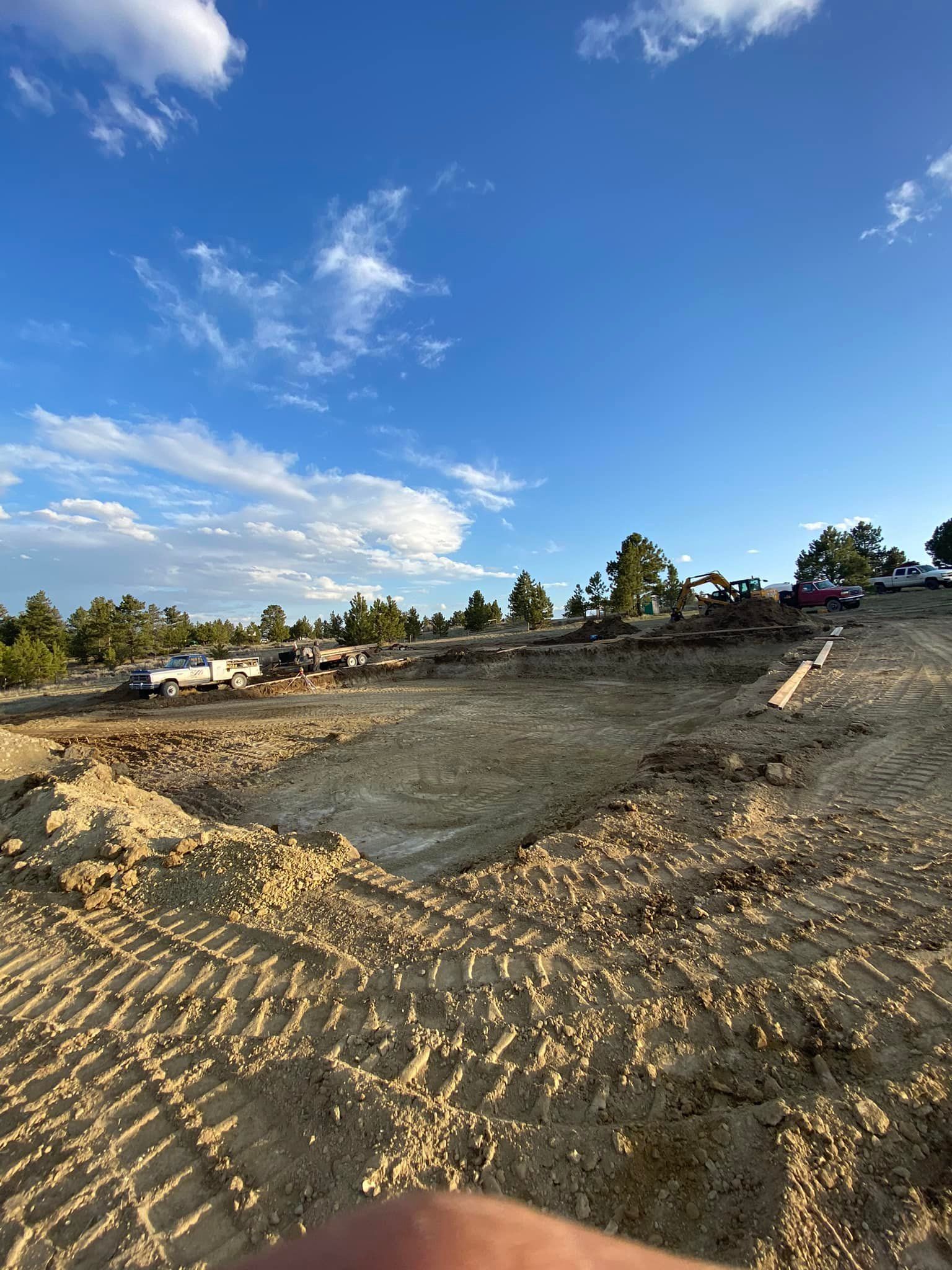Construction site with exposed earth, heavy machinery, and blue sky with clouds.
