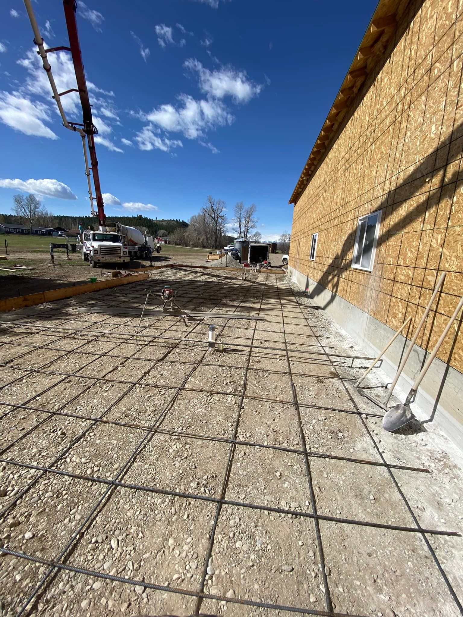 Construction site: Concrete pour in progress; rebar grid on gravel. Concrete pump truck, building exterior, blue sky.
