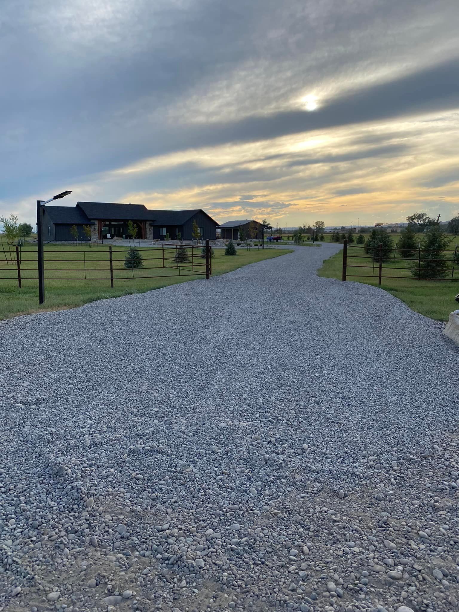 Gravel driveway leading to a long, low house under a cloudy sky.