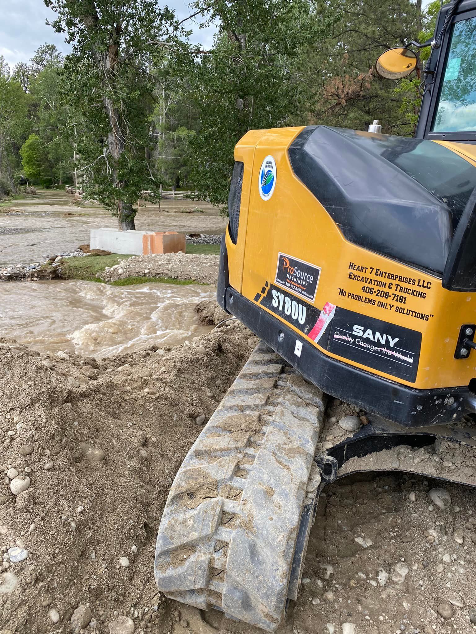 Yellow excavator track in muddy dirt near a shallow water stream.