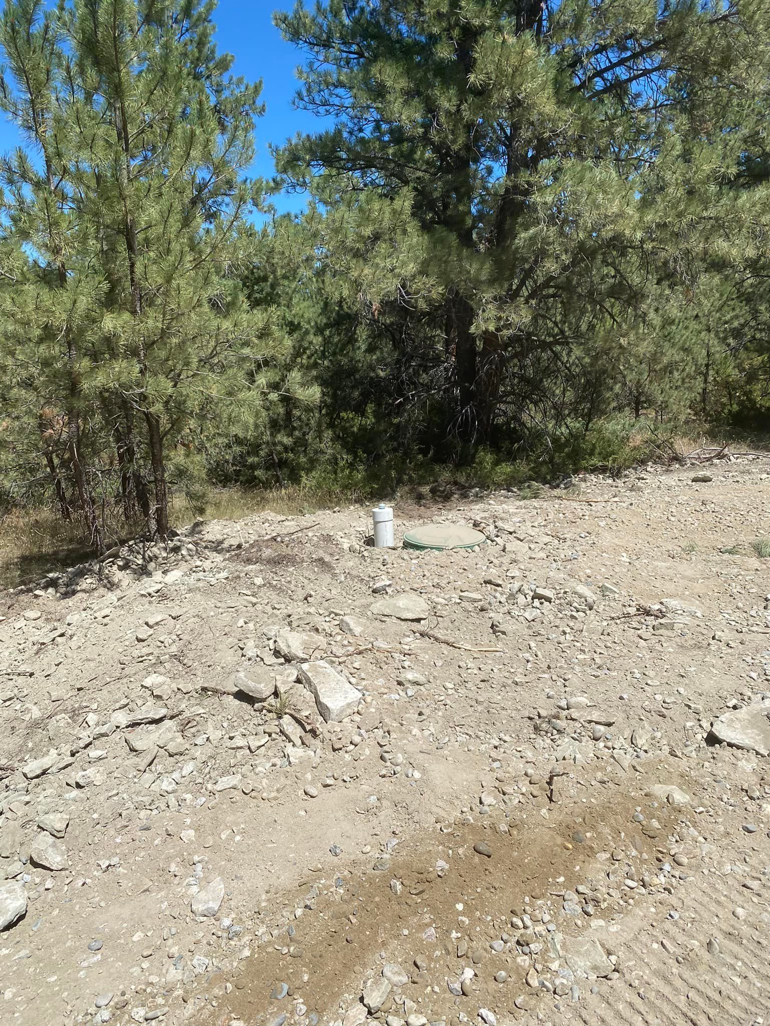Gravel ground with a white cylinder in the center. Trees in the background against a blue sky.
