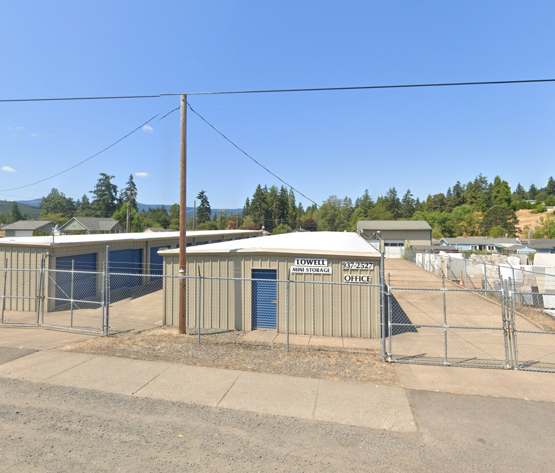 Storage units behind a chain link fence; tan buildings, blue doors, sunny day.