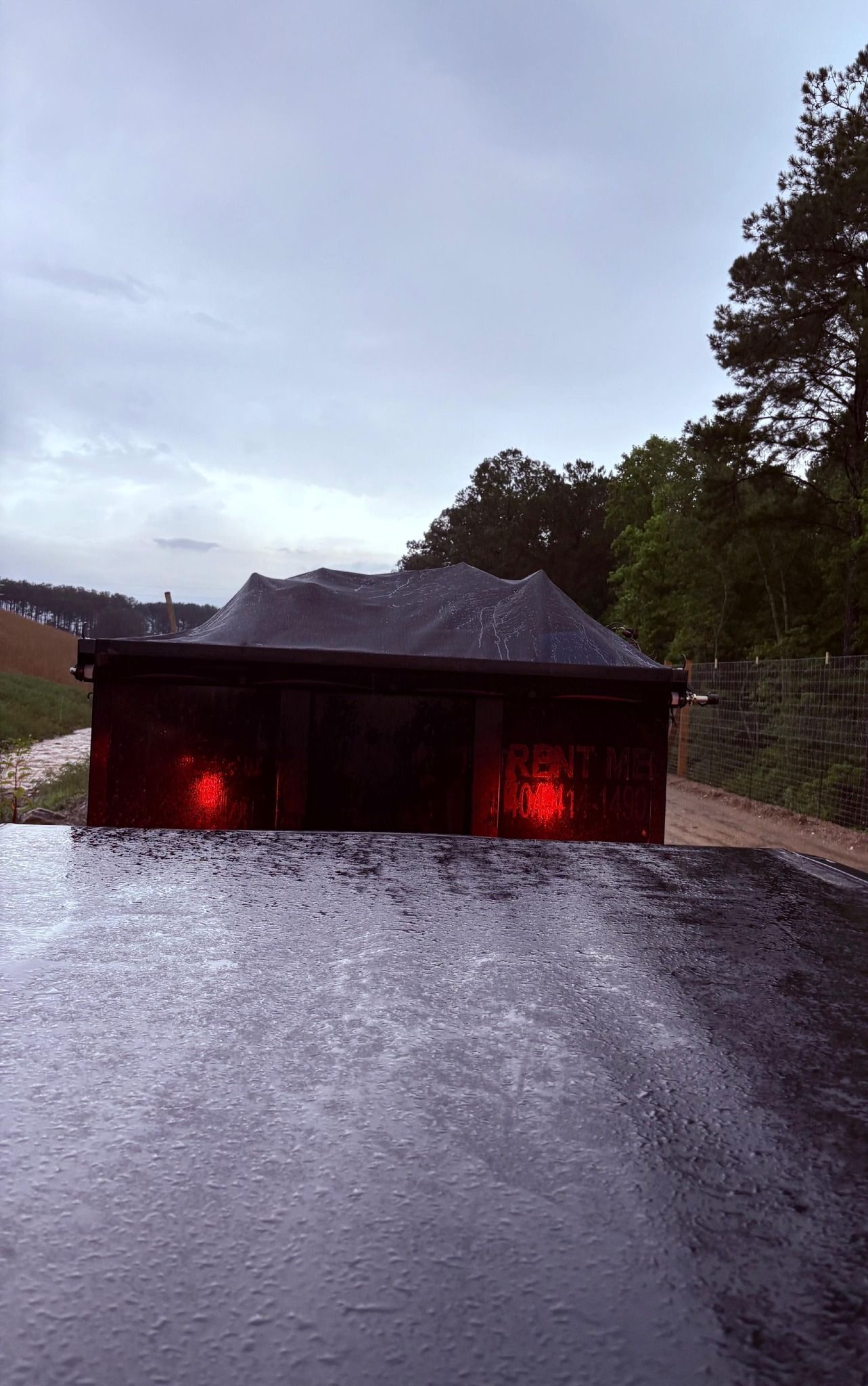 Rear view of a dark truck carrying a load, on a wet dirt road under an overcast sky.