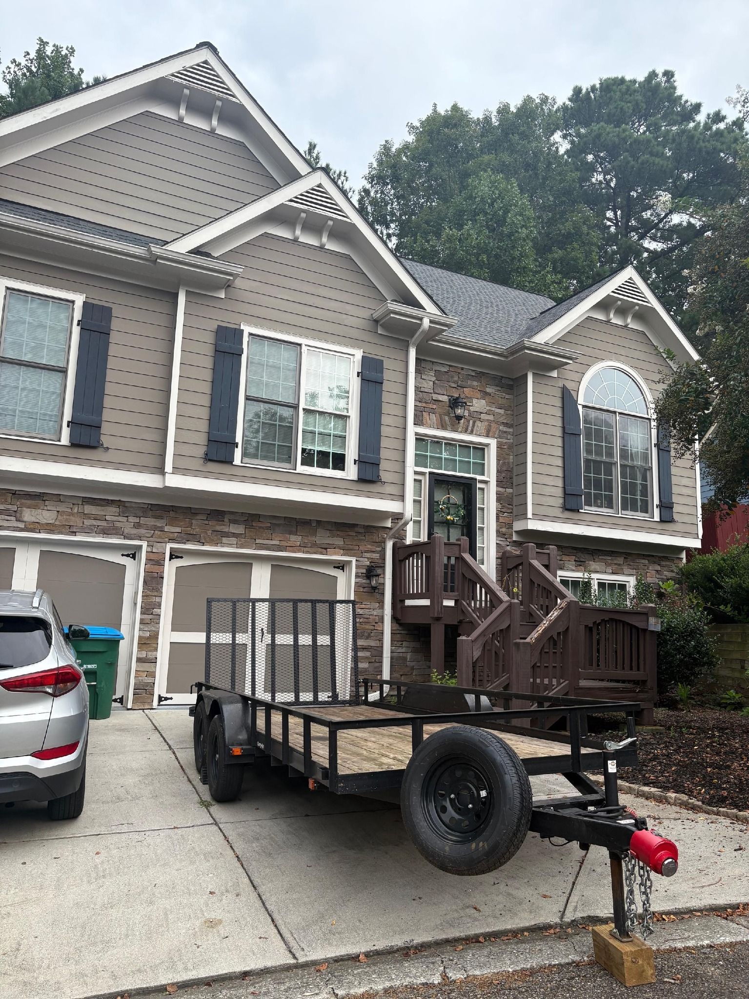 Two-story house with a parked trailer in the driveway. Tan siding, stone facade, and dark shutters.