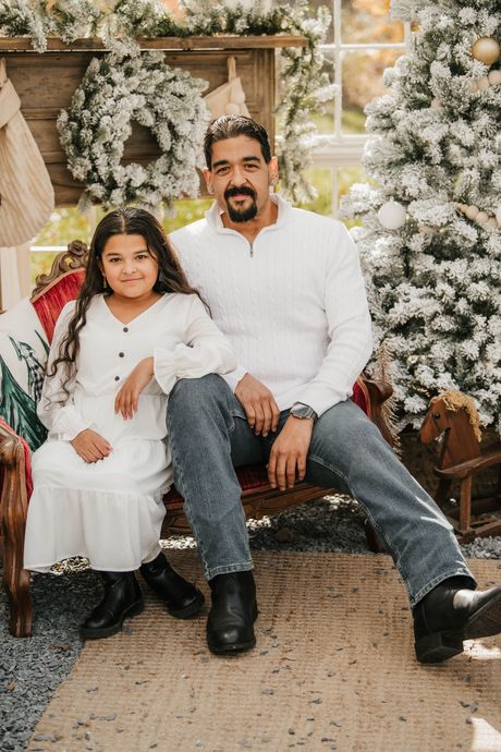 Father and daughter sit together, both in white, in a Christmas setting.