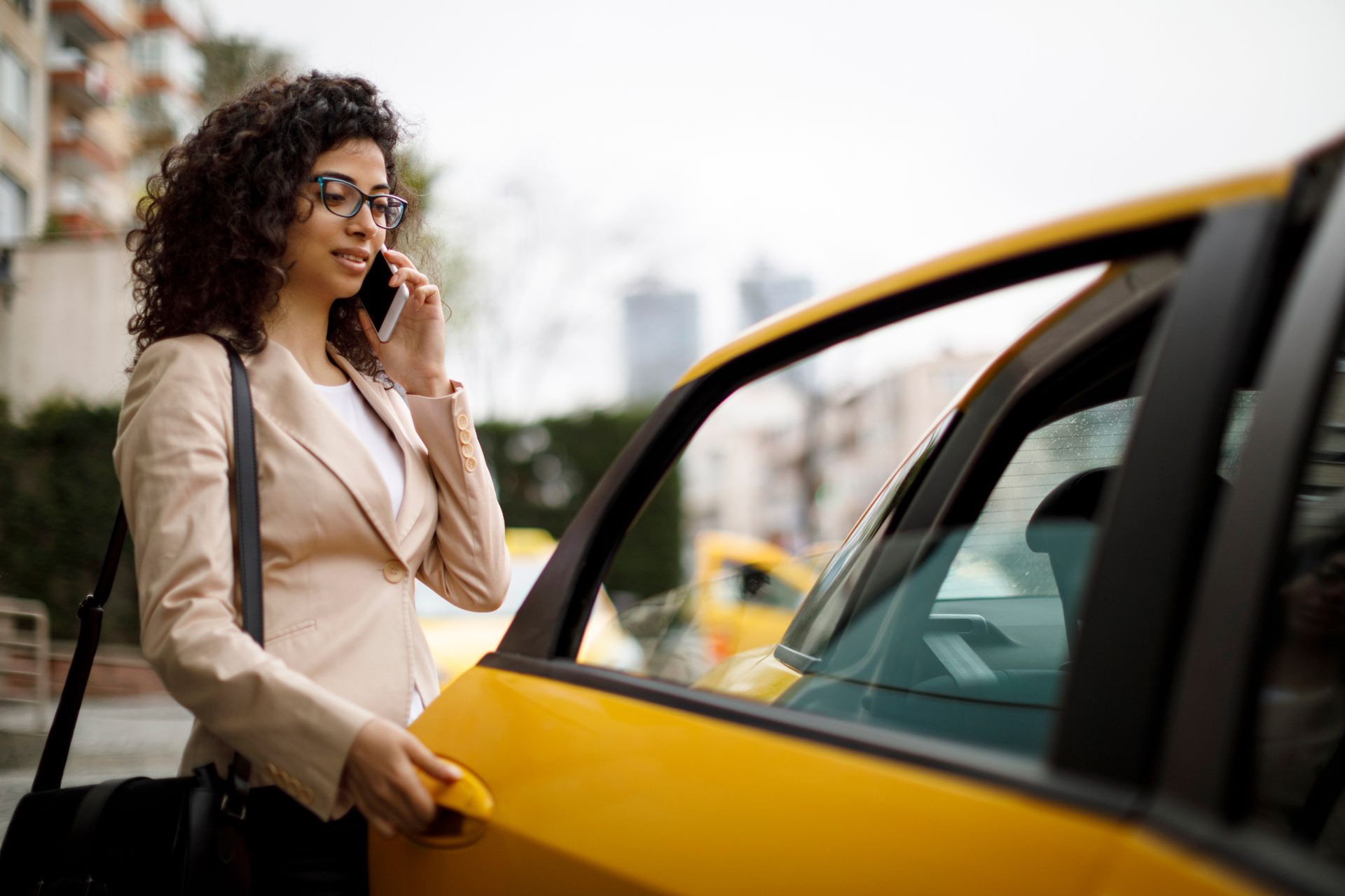 A woman is talking on a cell phone while getting out of a taxi.