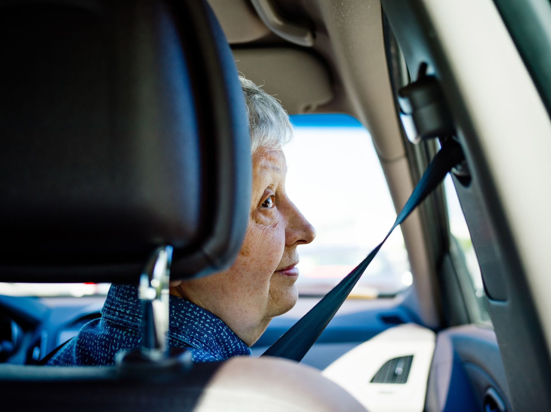 An elderly woman is sitting in a car with her seat belt on.