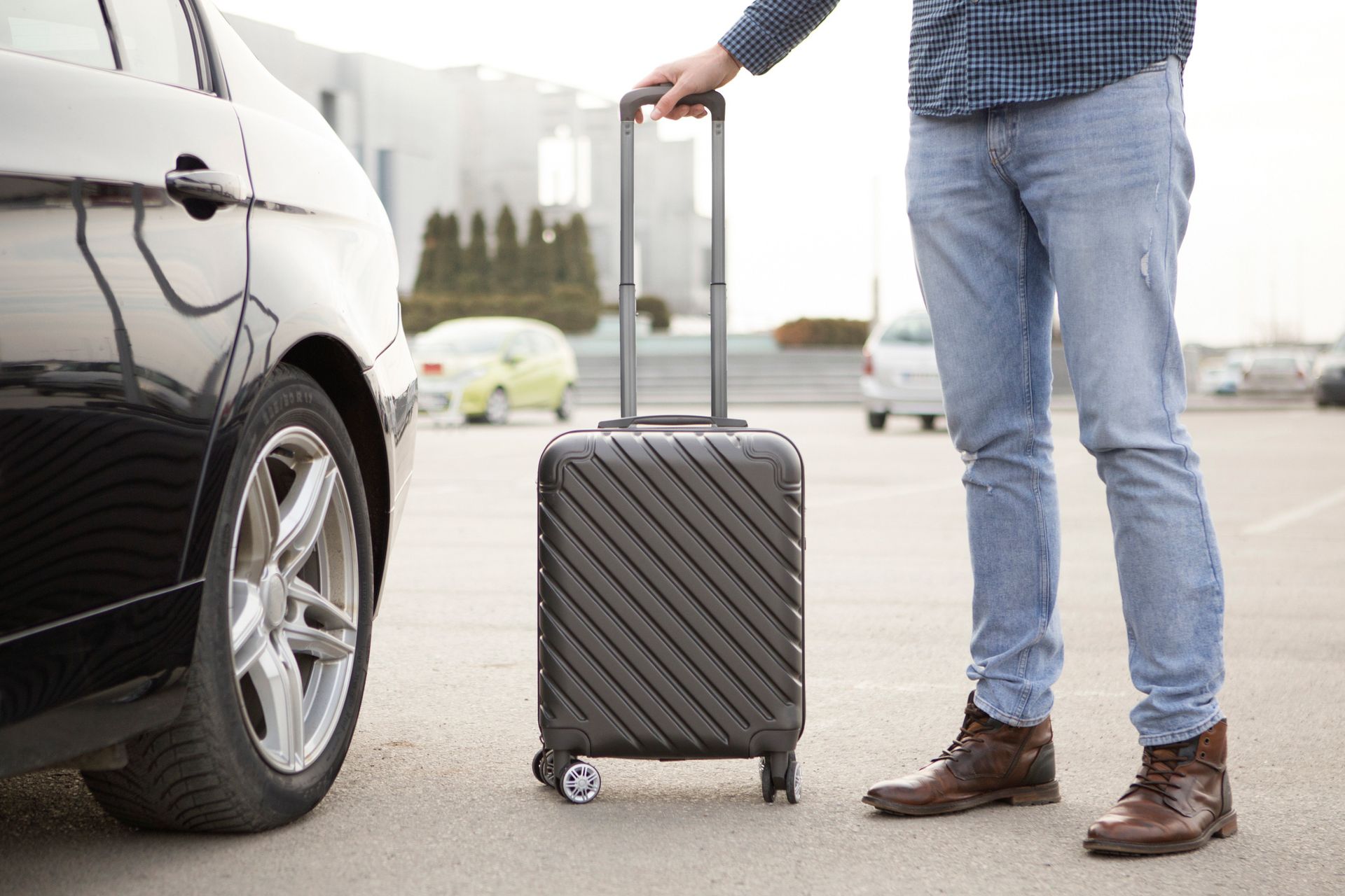 A man is holding a suitcase next to a car in a parking lot.
