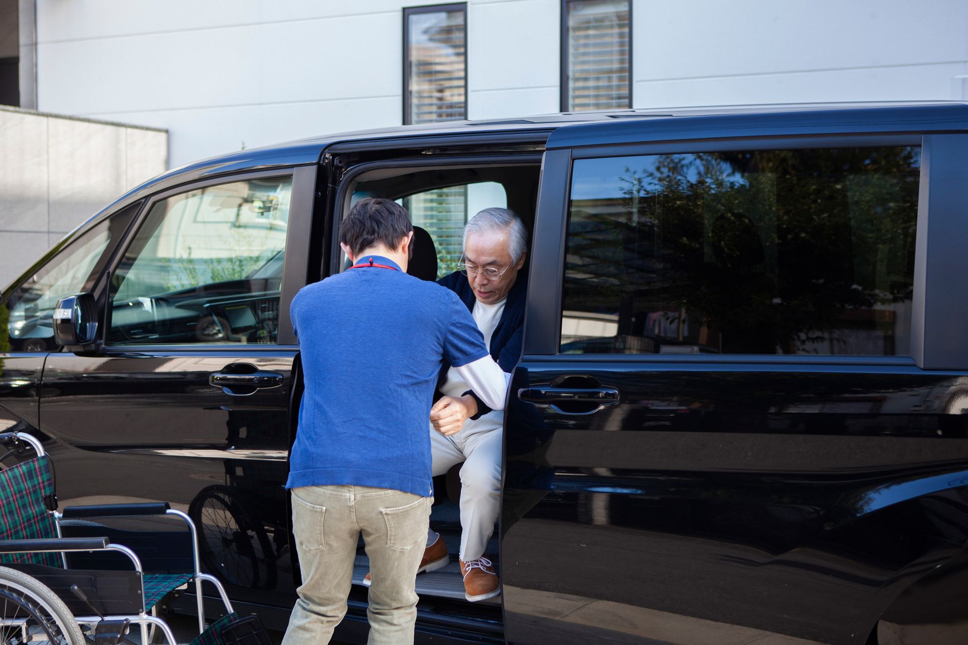 A man is helping an elderly woman get out of a van.