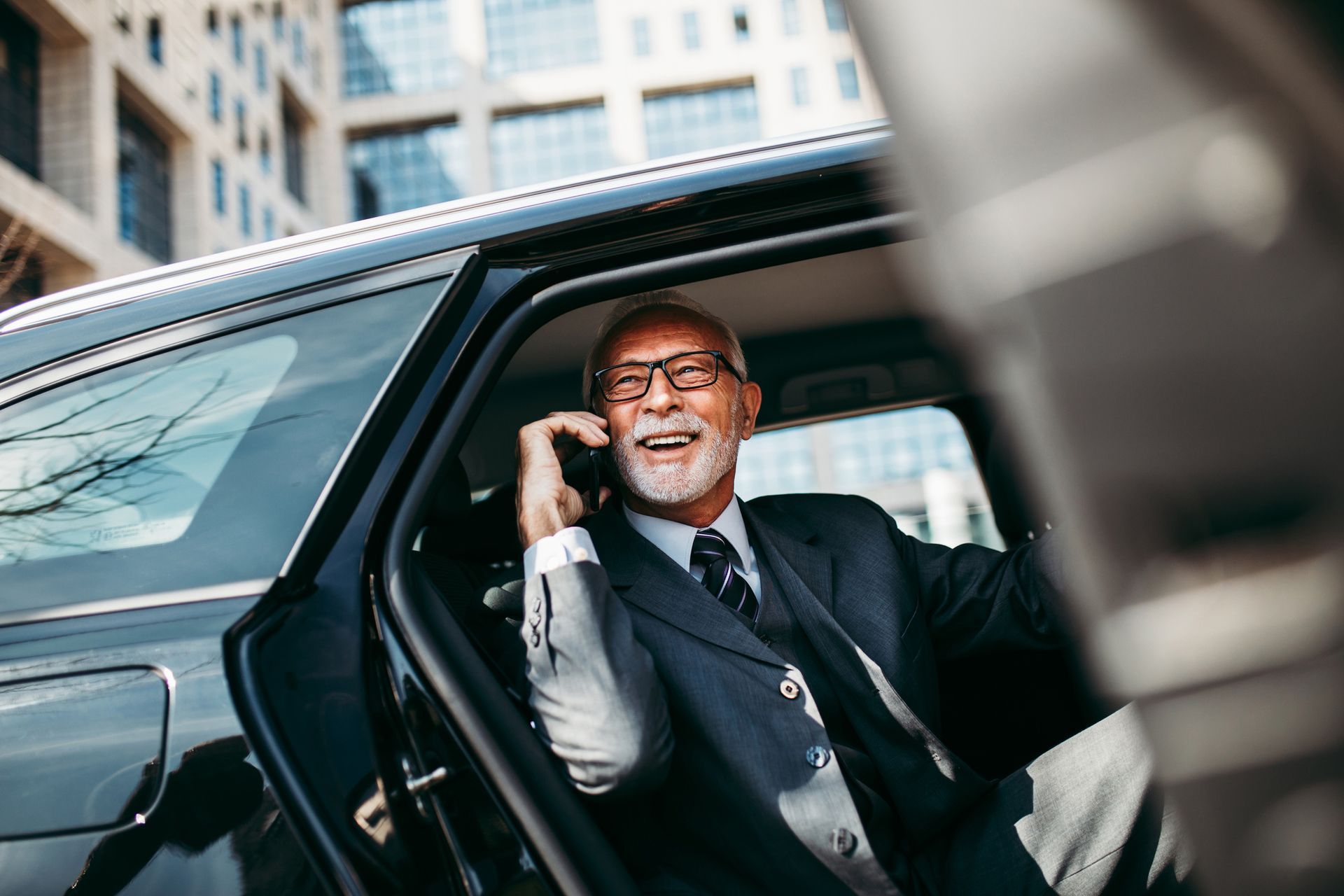 An older man is sitting in the back seat of a car talking on a cell phone.