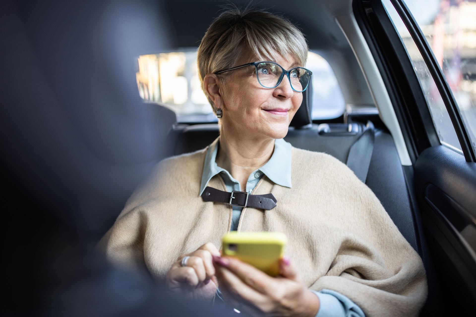 An older woman is sitting in the back seat of a car using a cell phone.
