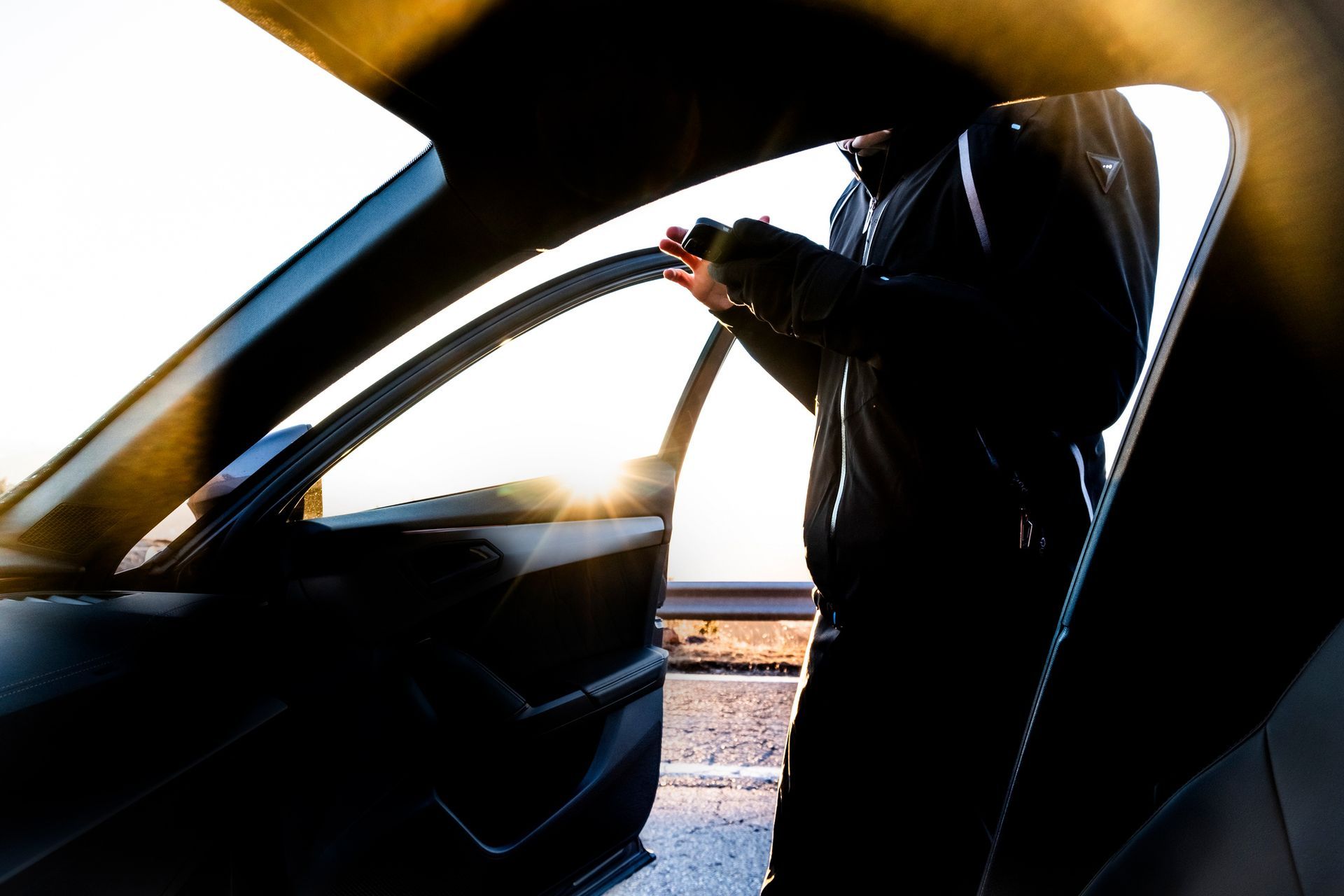 A man is getting out of a car and looking at his phone.
