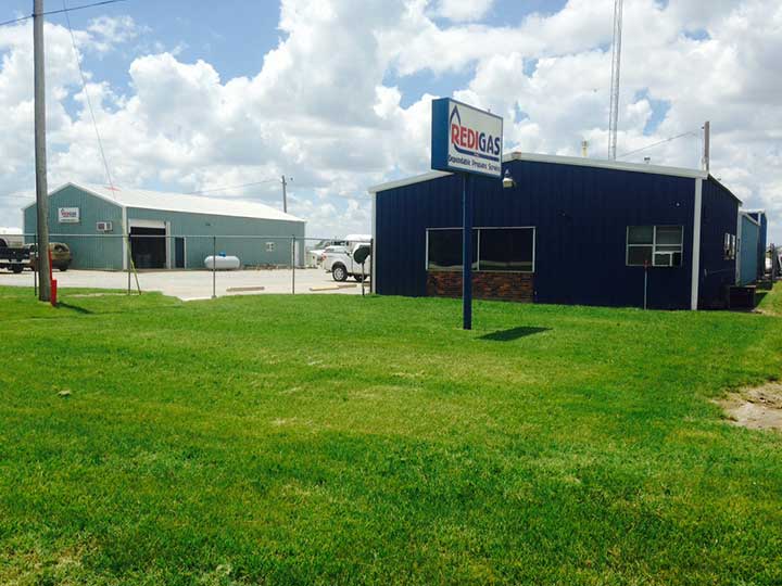 Blue Redgas propane service building with sign, adjacent to a gray storage building, green grass, and blue sky.